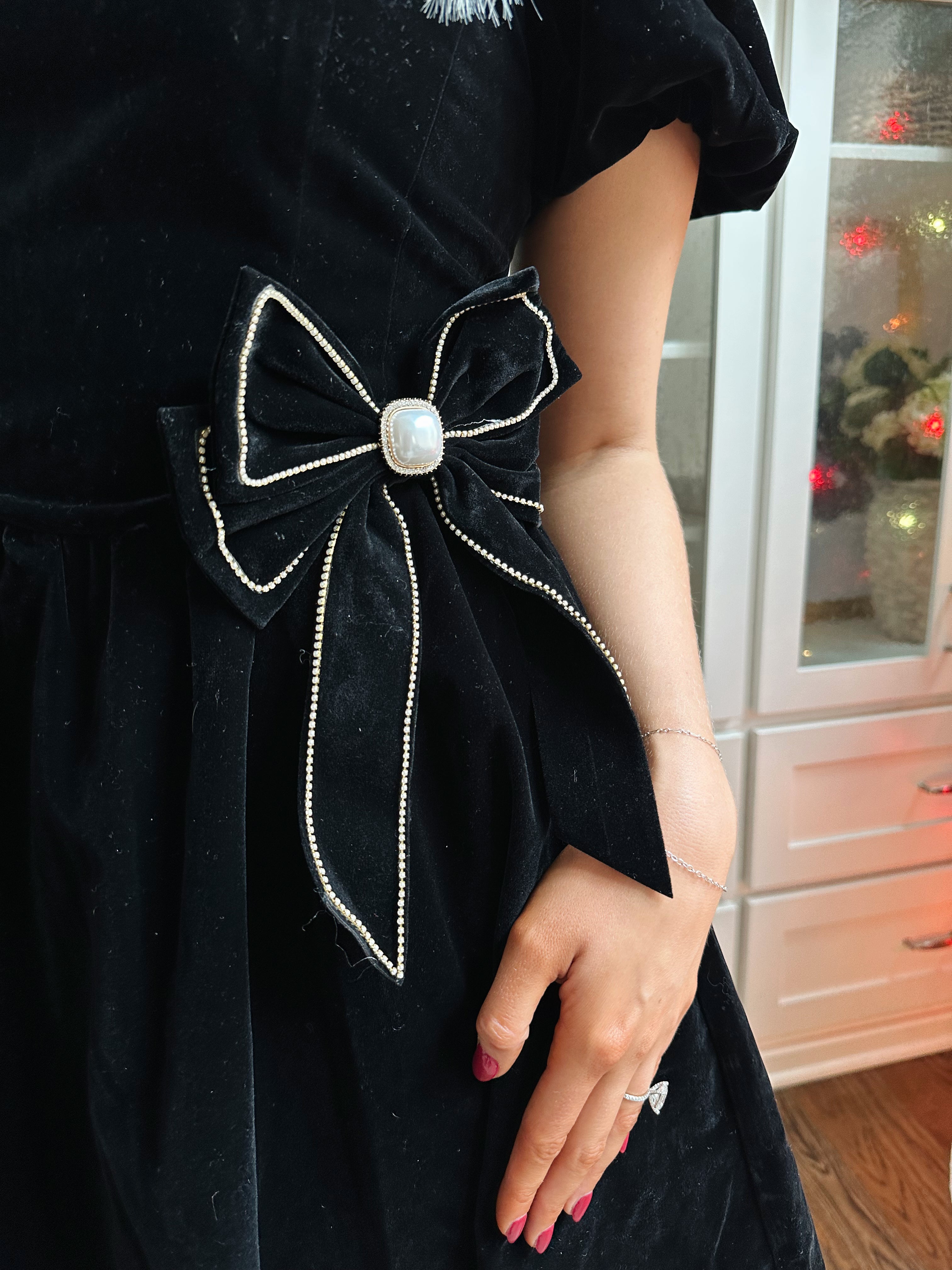 Woman wearing black velvet babydoll mini dress with puff sleeves, and bow detailing. 