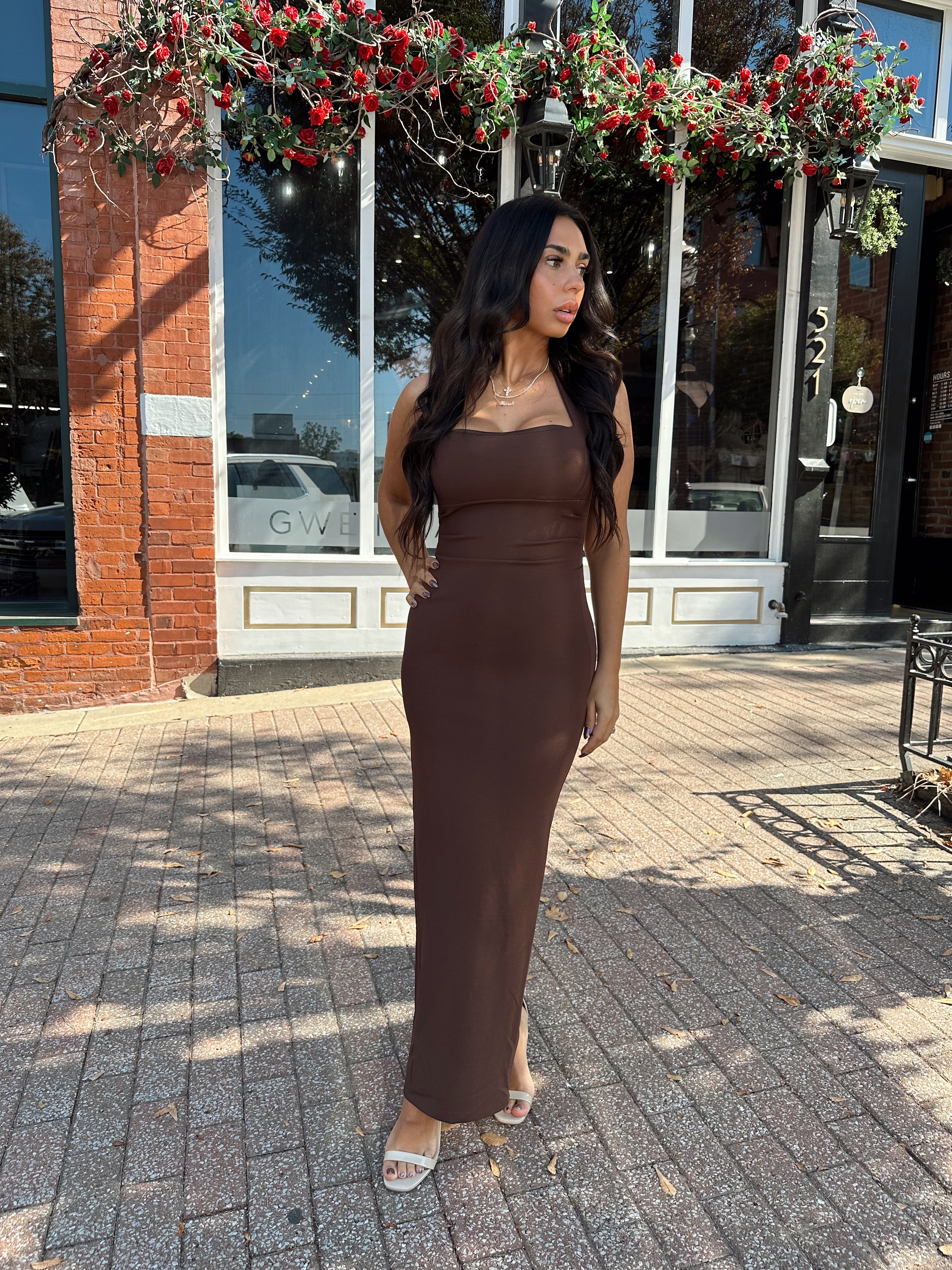 Woman wearing brown fitted square neck midi dress with slit in the back.