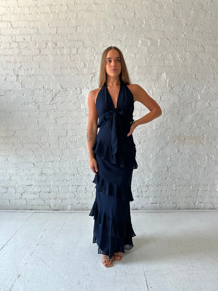 Woman wearing navy blue halter maxi dress with ruffle tiered detailing. 