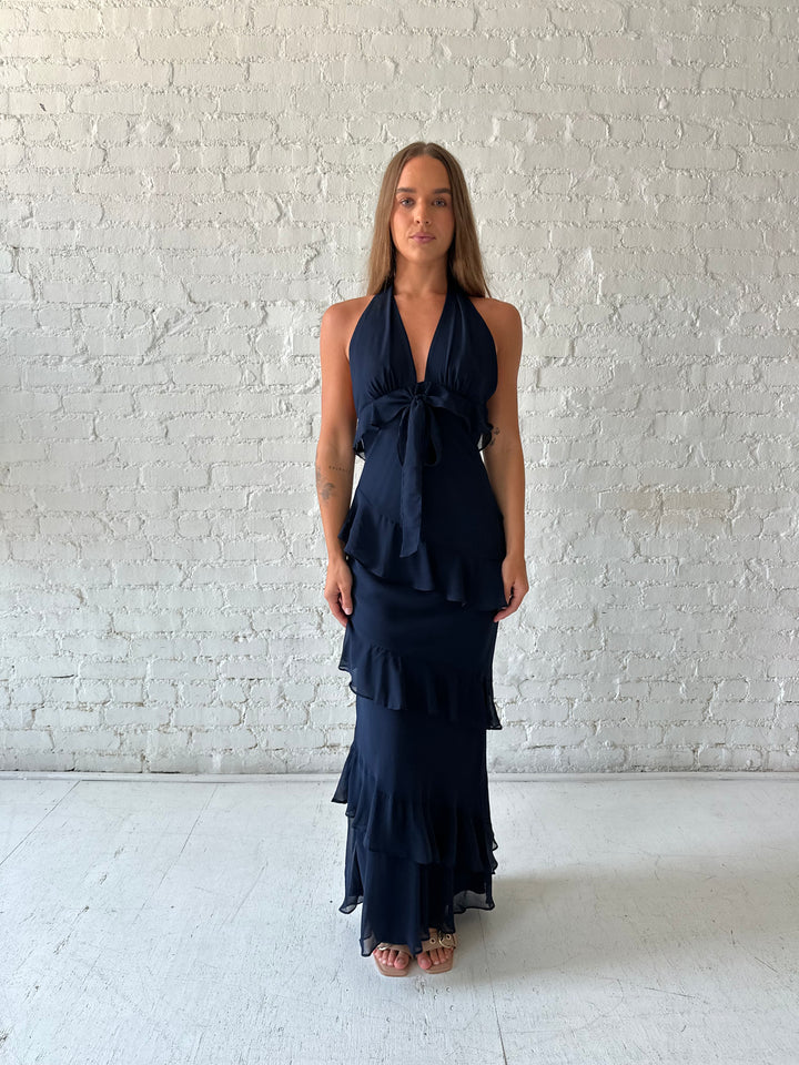 Woman wearing navy blue halter maxi dress with ruffle tiered detailing. 