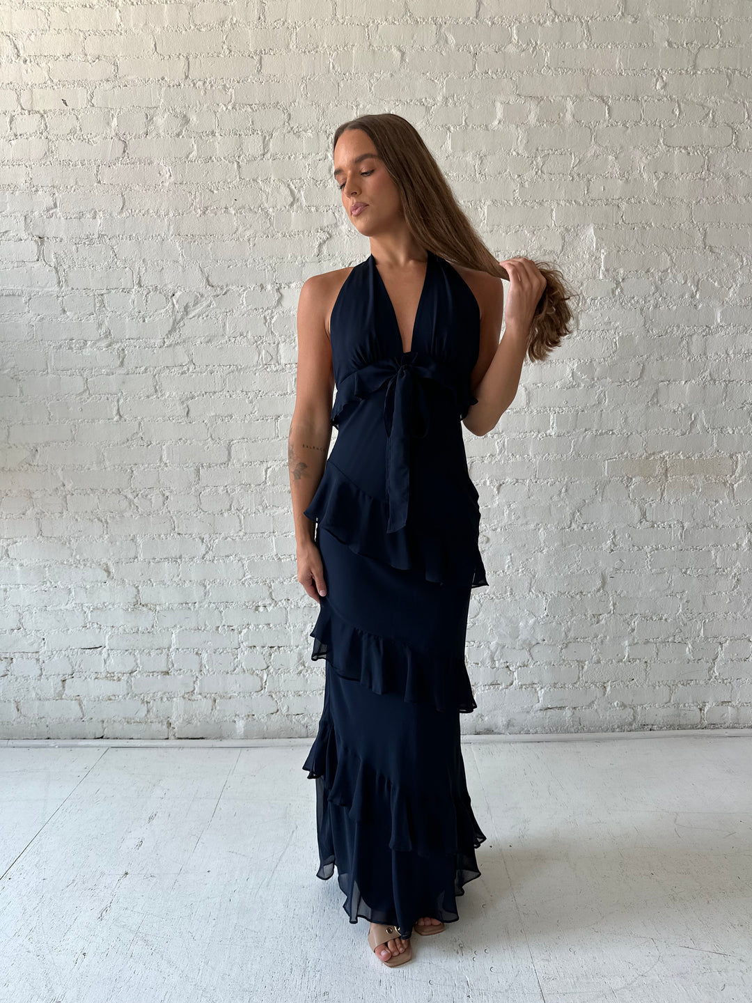 Woman wearing navy blue halter maxi dress with ruffle tiered detailing. 