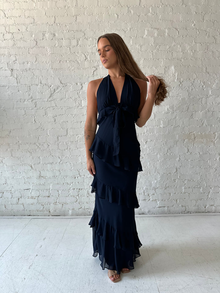 Woman wearing navy blue halter maxi dress with ruffle tiered detailing. 