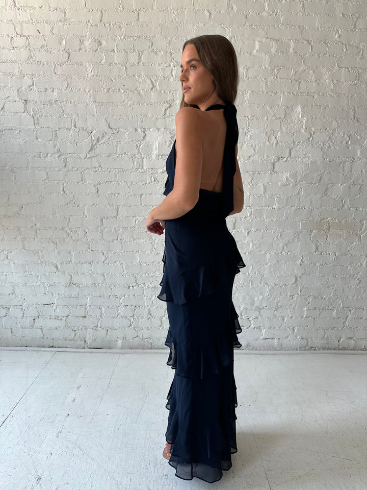 Woman wearing navy blue halter maxi dress with ruffle tiered detailing. 