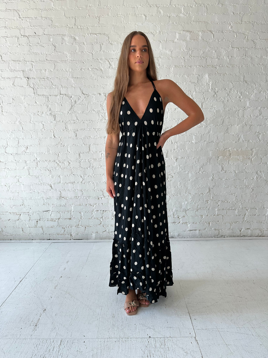Woman wearing black polka dot maxi dress with self tie halter neckline, and open back with tie detail.
