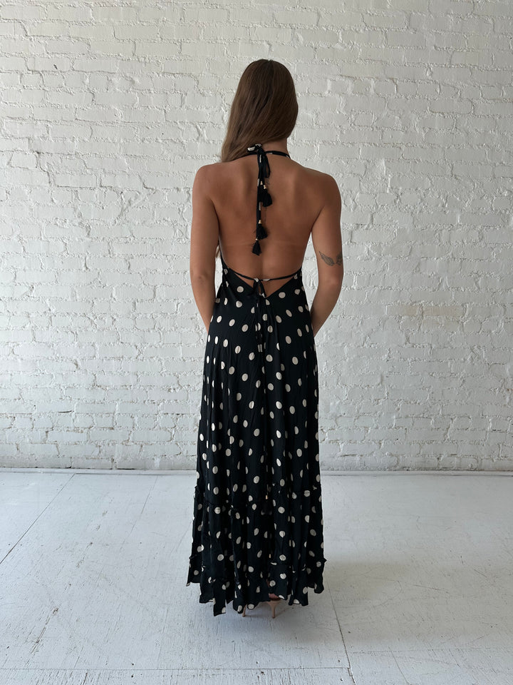 Woman wearing black polka dot maxi dress with self tie halter neckline, and open back with tie detail.