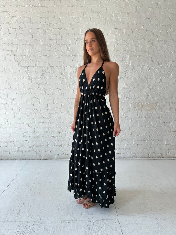 Woman wearing black polka dot maxi dress with self tie halter neckline, and open back with tie detail.