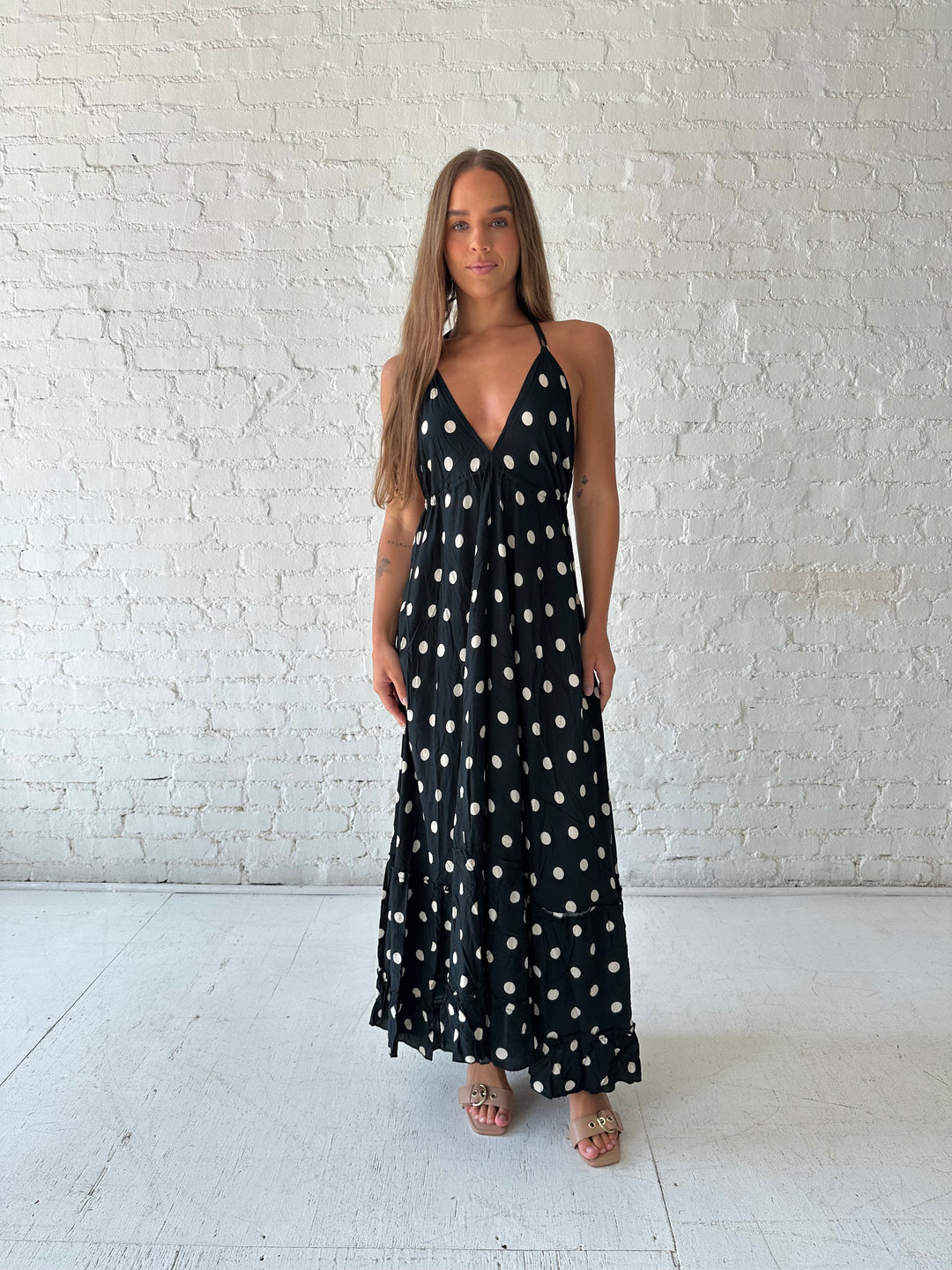 Woman wearing black polka dot maxi dress with self tie halter neckline, and open back with tie detail.
