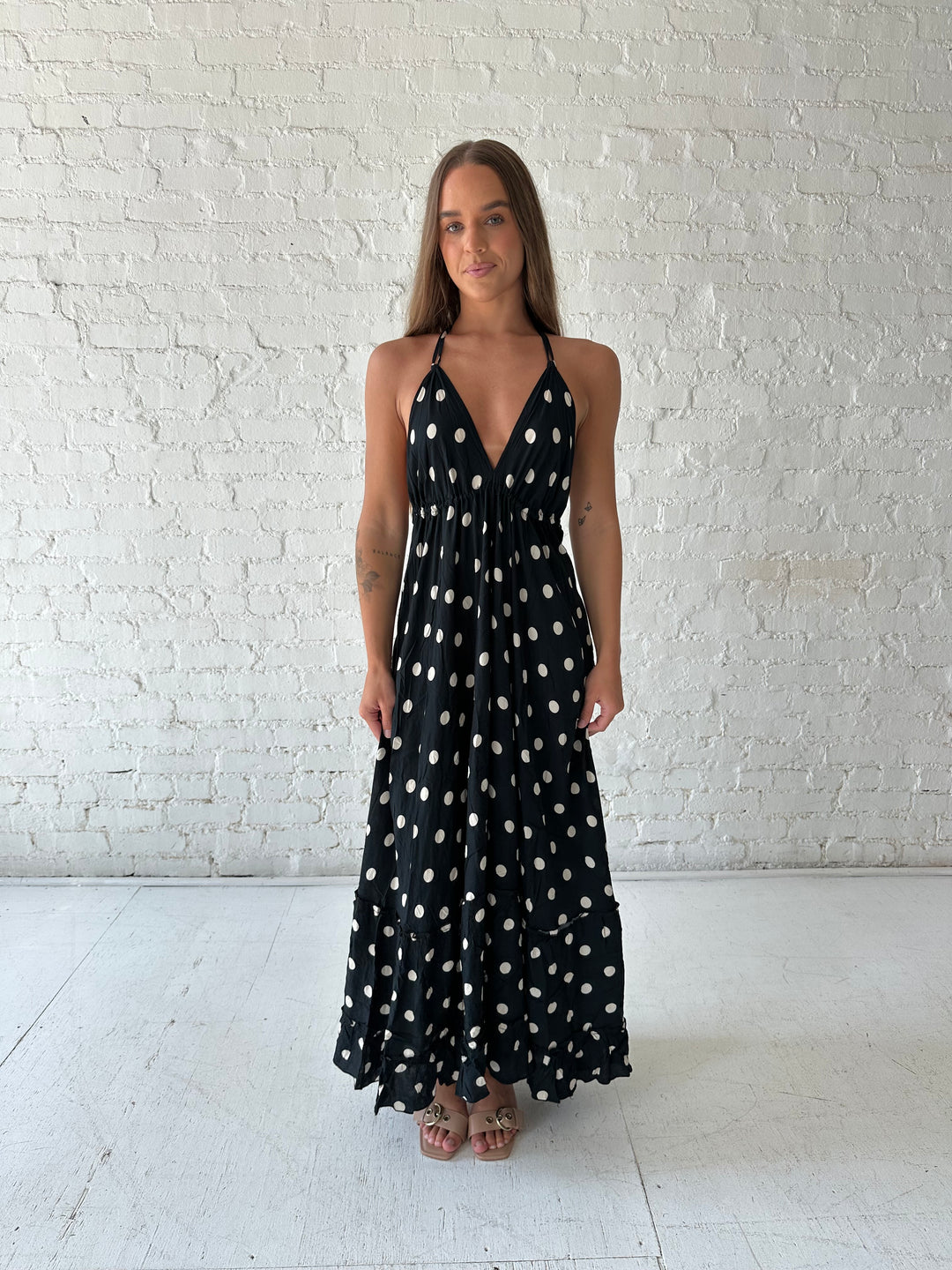 Woman wearing black polka dot maxi dress with self tie halter neckline, and open back with tie detail.
