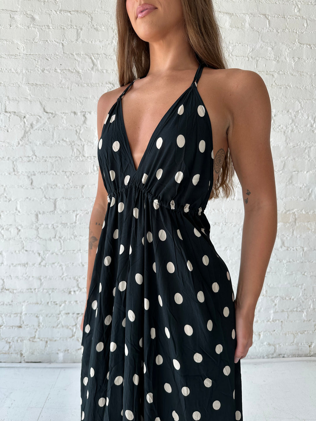 Woman wearing black polka dot maxi dress with self tie halter neckline, and open back with tie detail.