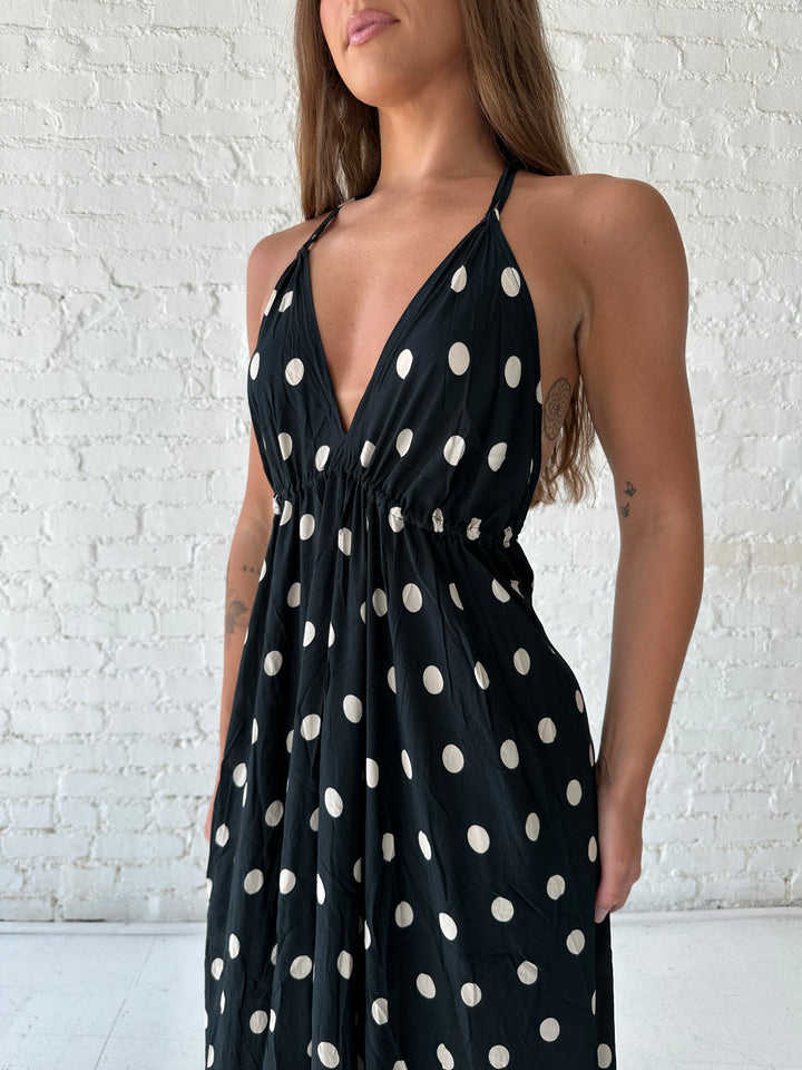 Woman wearing black polka dot maxi dress with self tie halter neckline, and open back with tie detail.