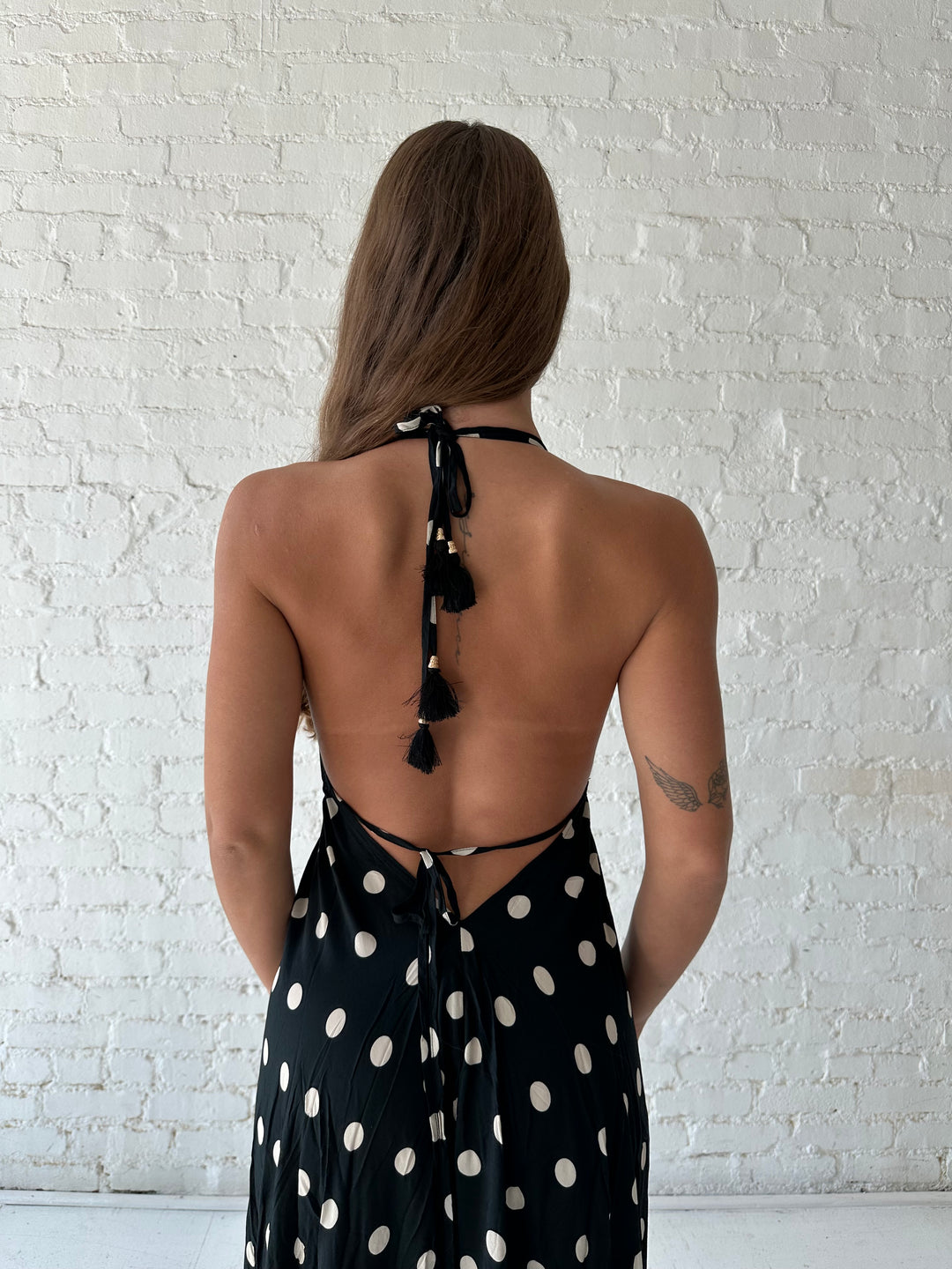 Woman wearing black polka dot maxi dress with self tie halter neckline, and open back with tie detail.