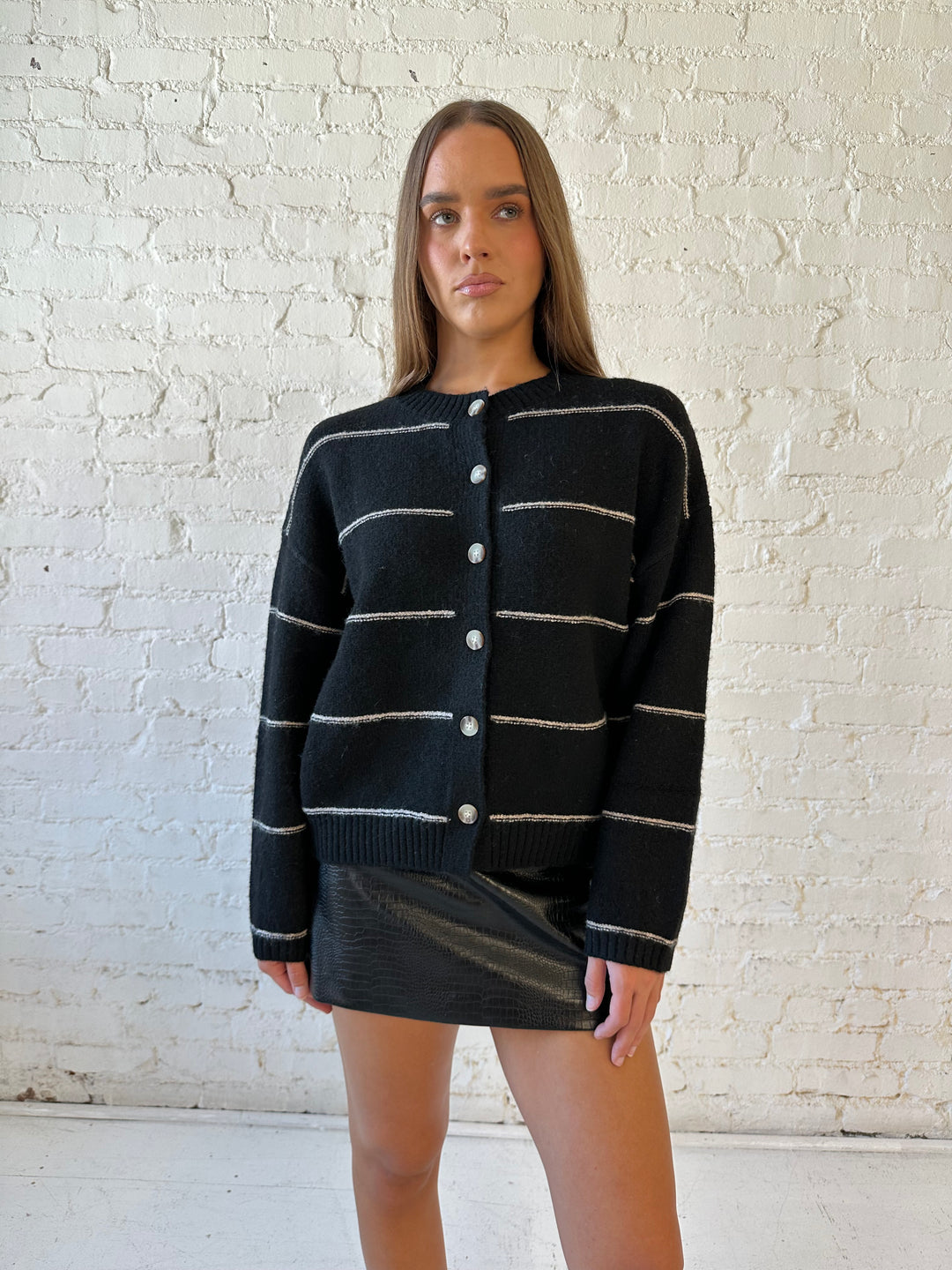 Woman wearing black chunky striped knit button down cardigan with high waisted leather mini skirt. 