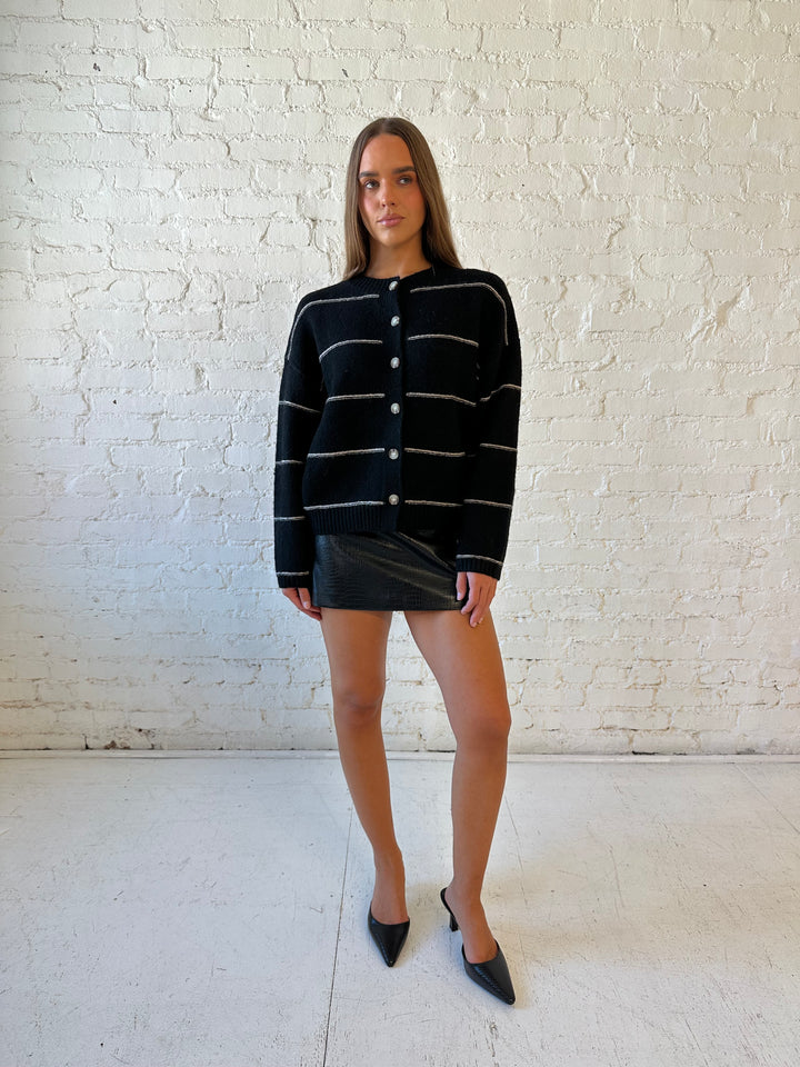 Woman wearing black chunky striped knit button down cardigan with high waisted leather mini skirt. 