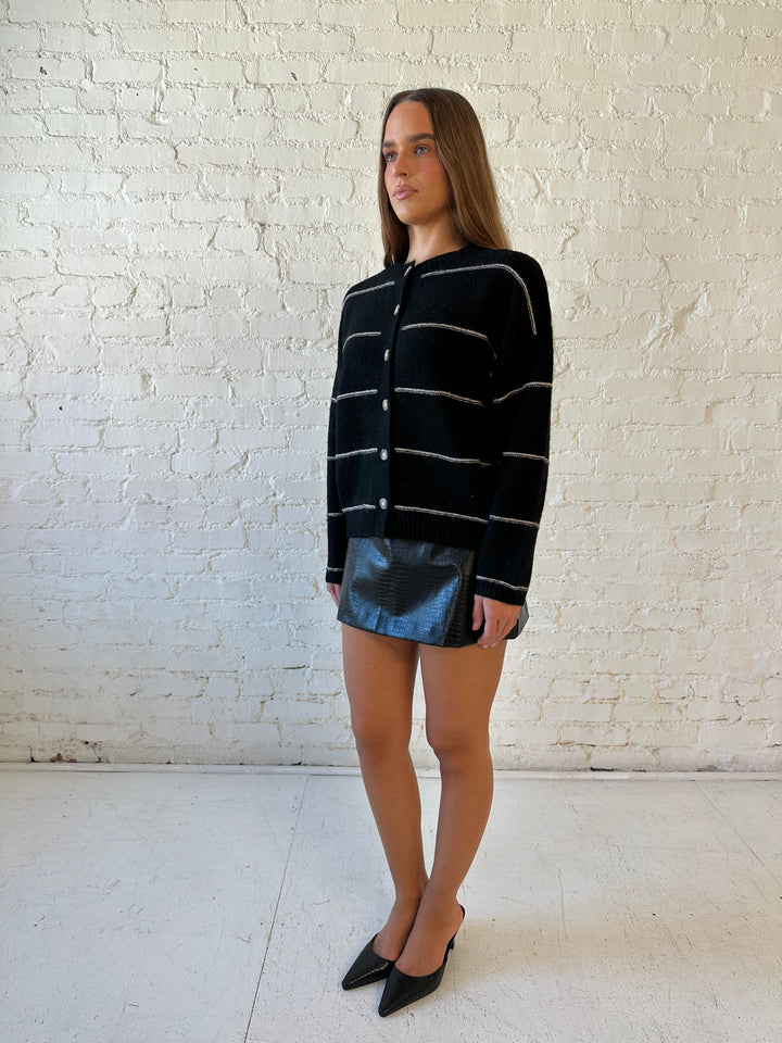 Woman wearing black chunky striped knit button down cardigan with high waisted leather mini skirt. 