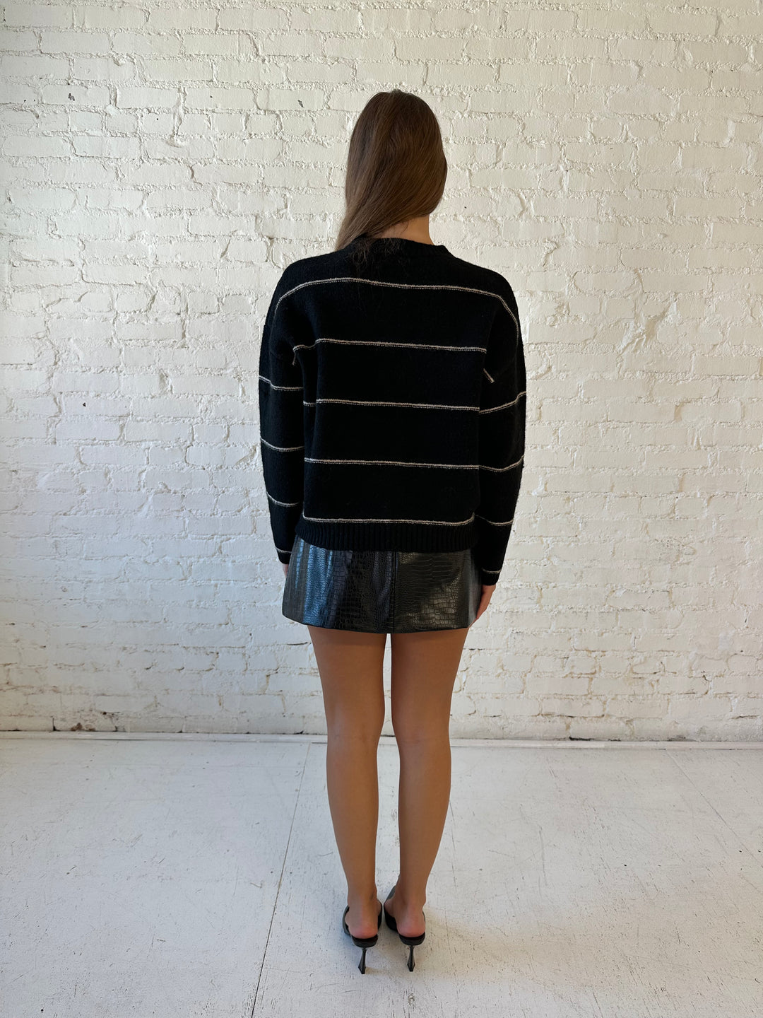 Woman wearing black chunky striped knit button down cardigan with high waisted leather mini skirt. 