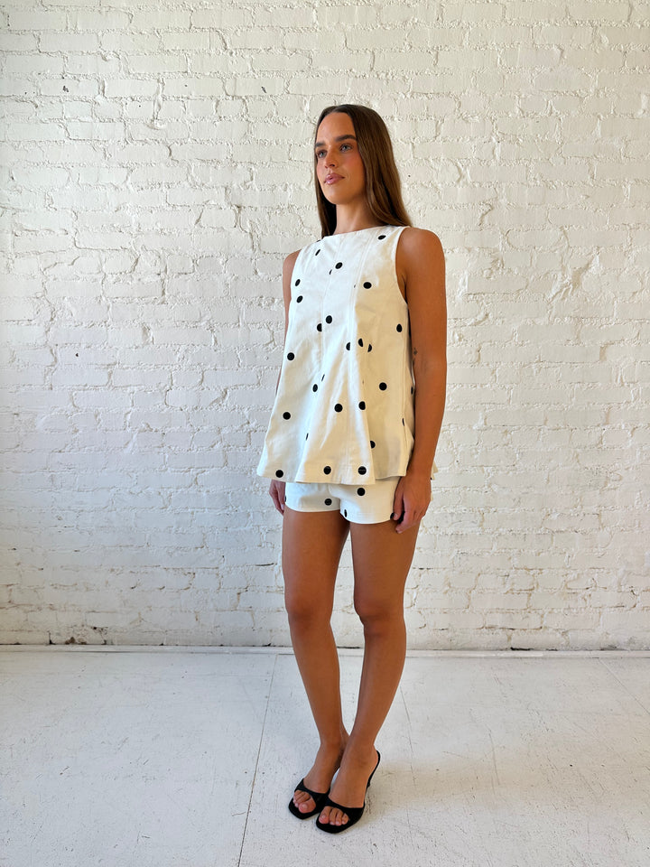 Woman wearing ivory polka dot set with black kitten heels.