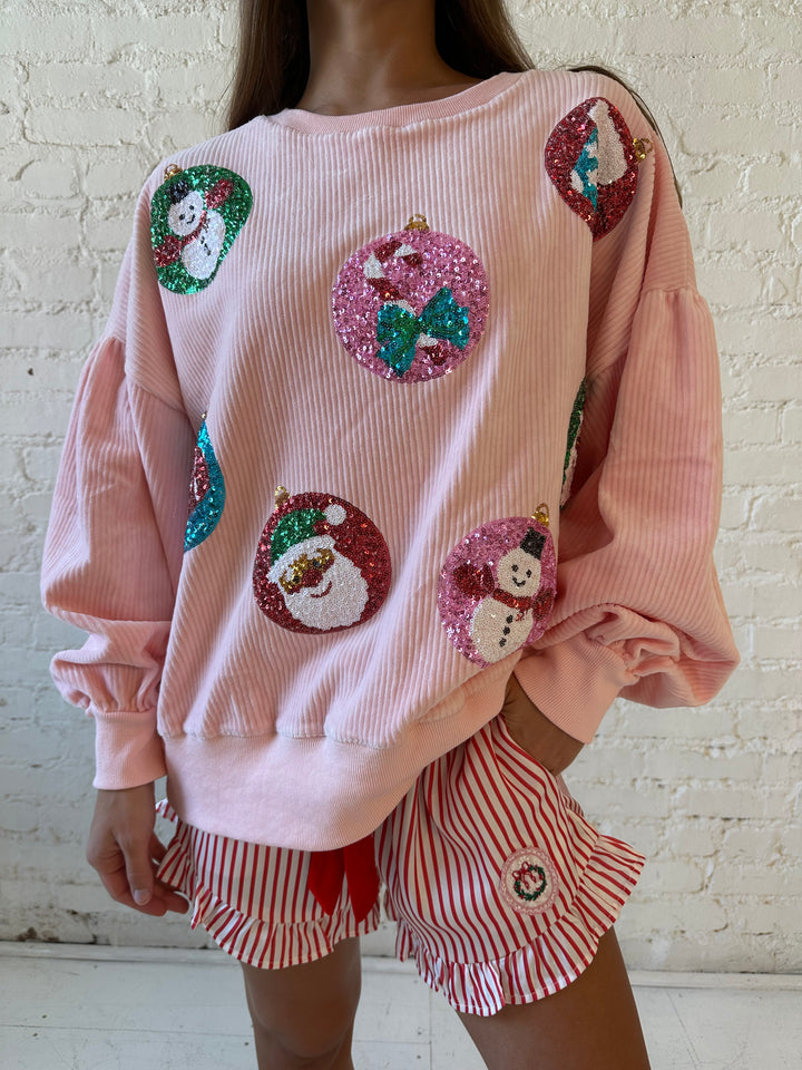 Woman wearing light pink ribbed oversized pull over with sequin ornaments all over. 