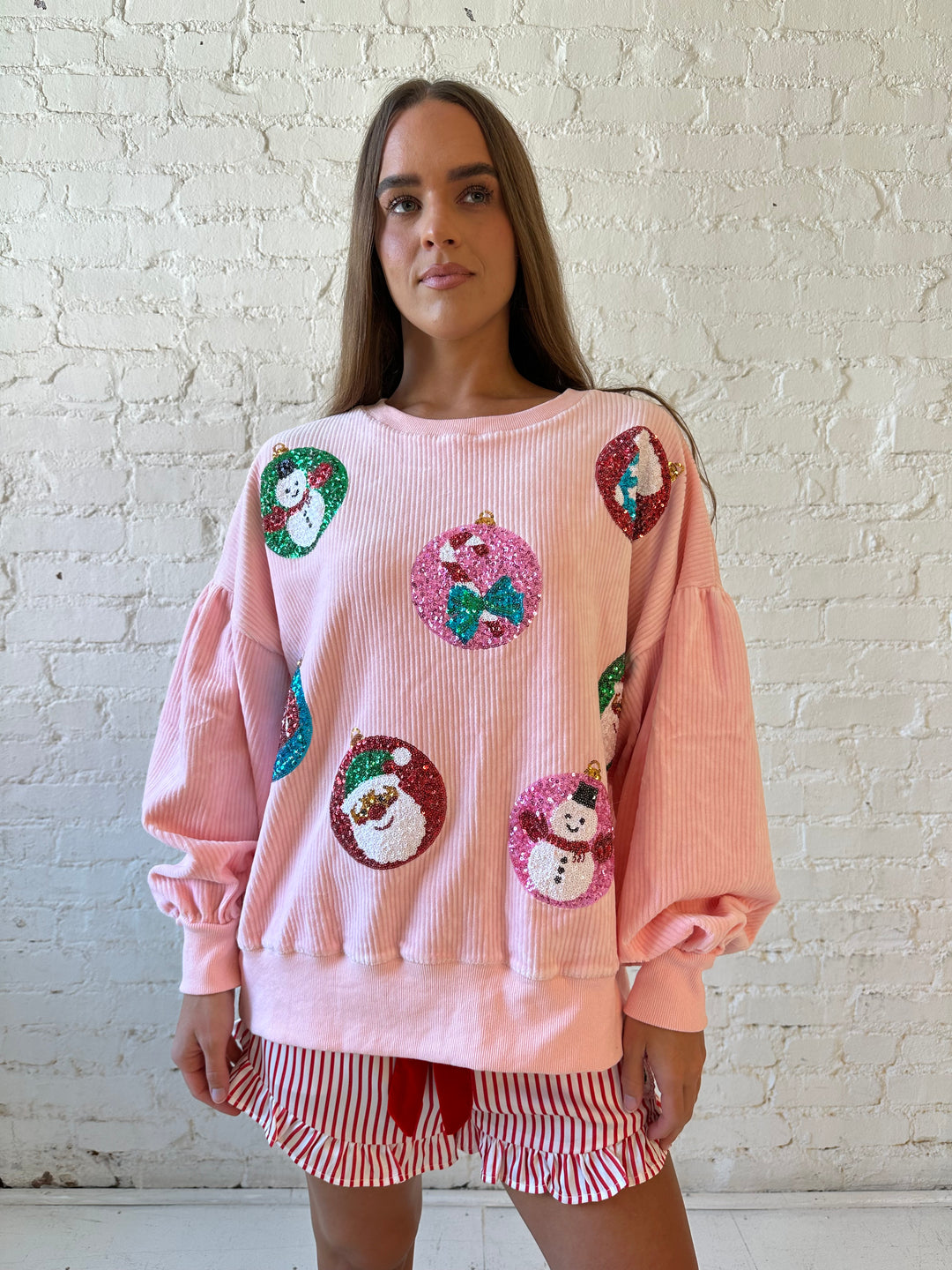 Woman wearing light pink ribbed oversized pull over with sequin ornaments all over. 