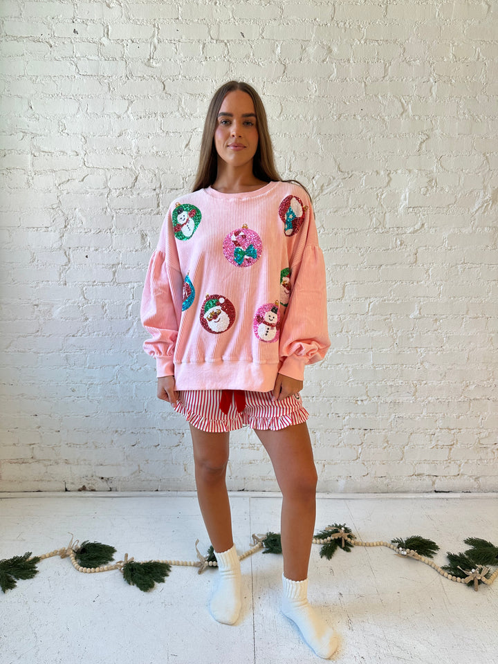 Woman wearing light pink ribbed oversized pull over with sequin ornaments all over. 