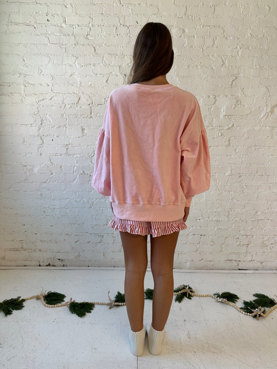 Woman wearing light pink ribbed oversized pull over with sequin ornaments all over. 