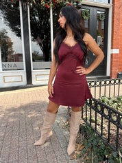 Woman wearing burgundy satin slip mini dress with lace detailing and adjustable straps.