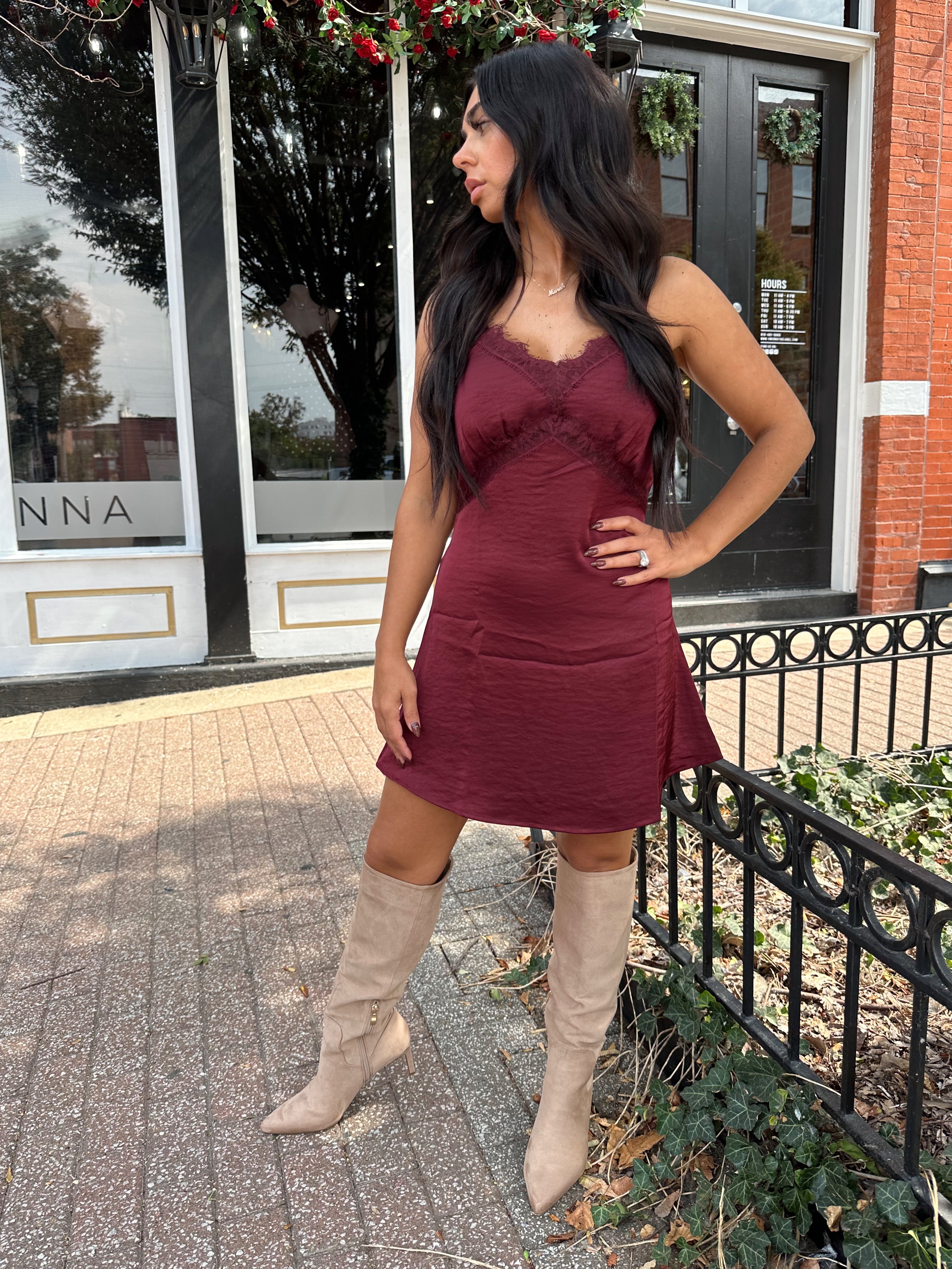 Woman wearing burgundy satin slip mini dress with lace detailing and adjustable straps.