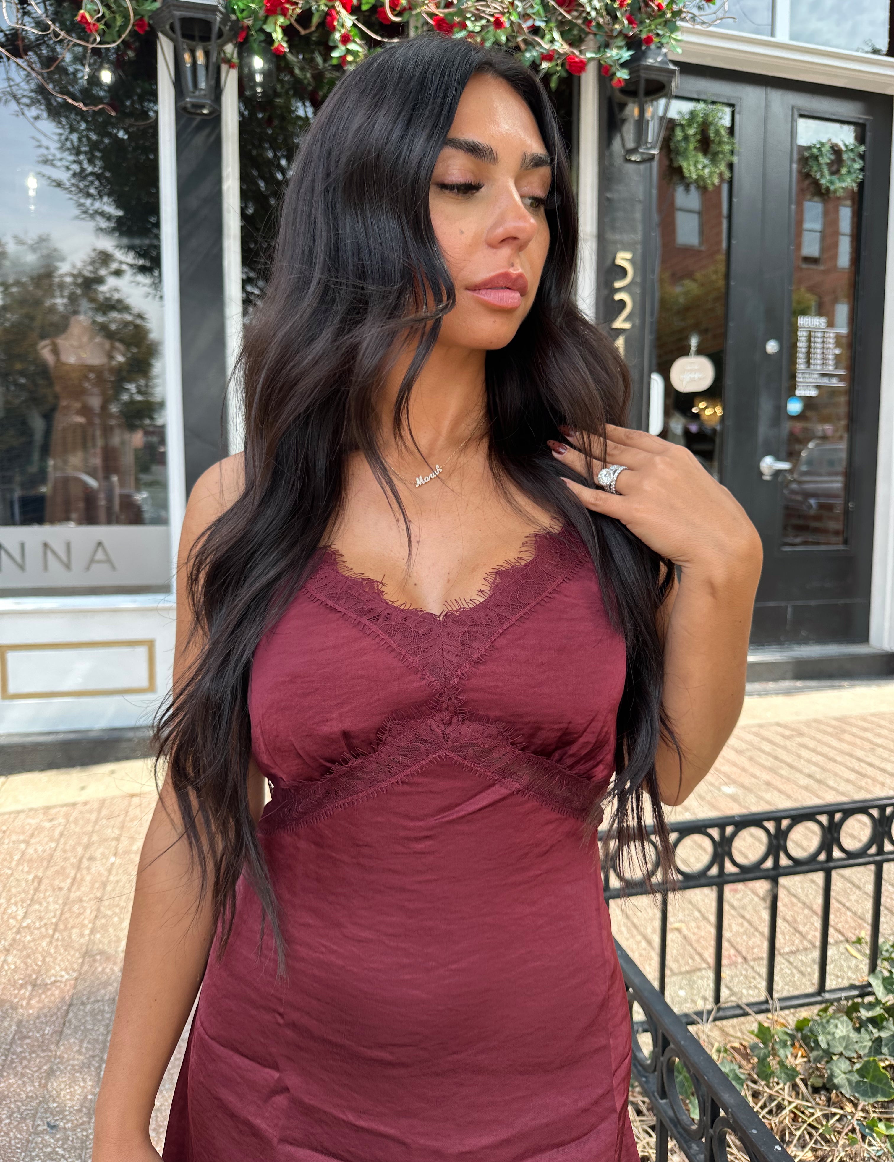 Woman wearing burgundy satin slip mini dress with lace detailing and adjustable straps.