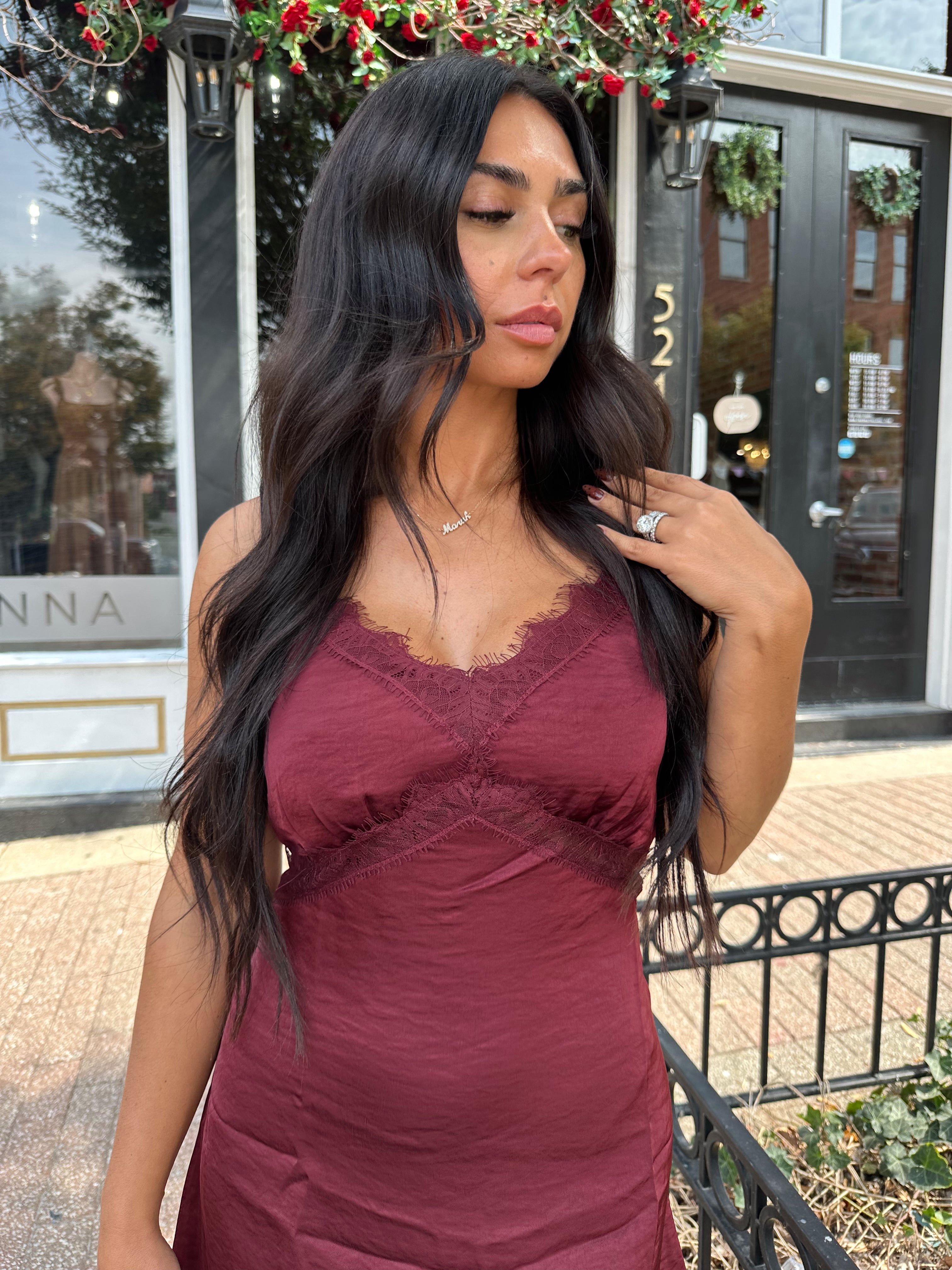Woman wearing burgundy satin slip mini dress with lace detailing and adjustable straps.