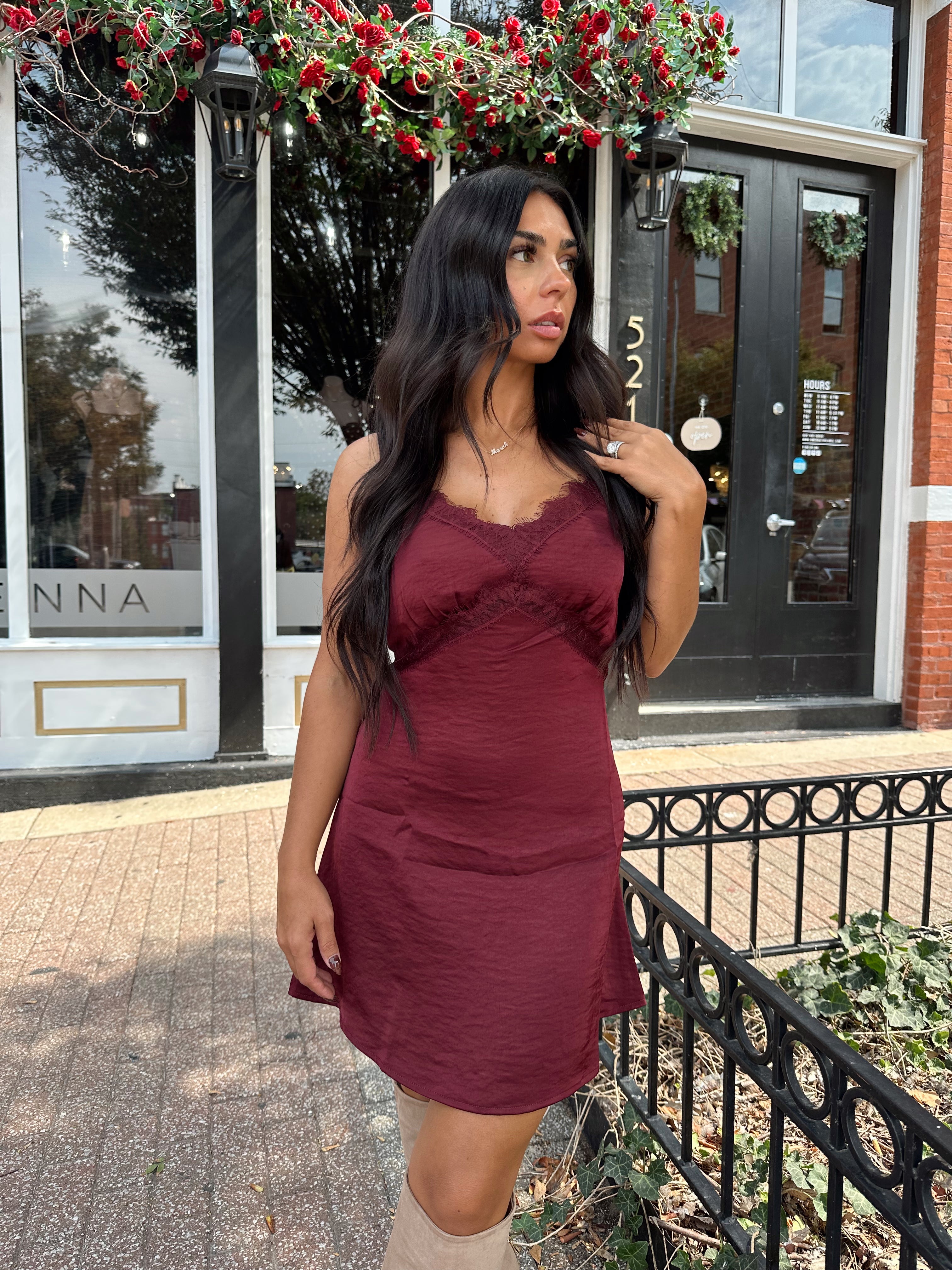 Woman wearing burgundy satin slip mini dress with lace detailing and adjustable straps.