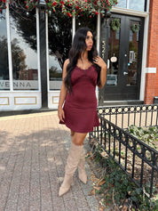Woman wearing burgundy satin slip mini dress with lace detailing and adjustable straps.