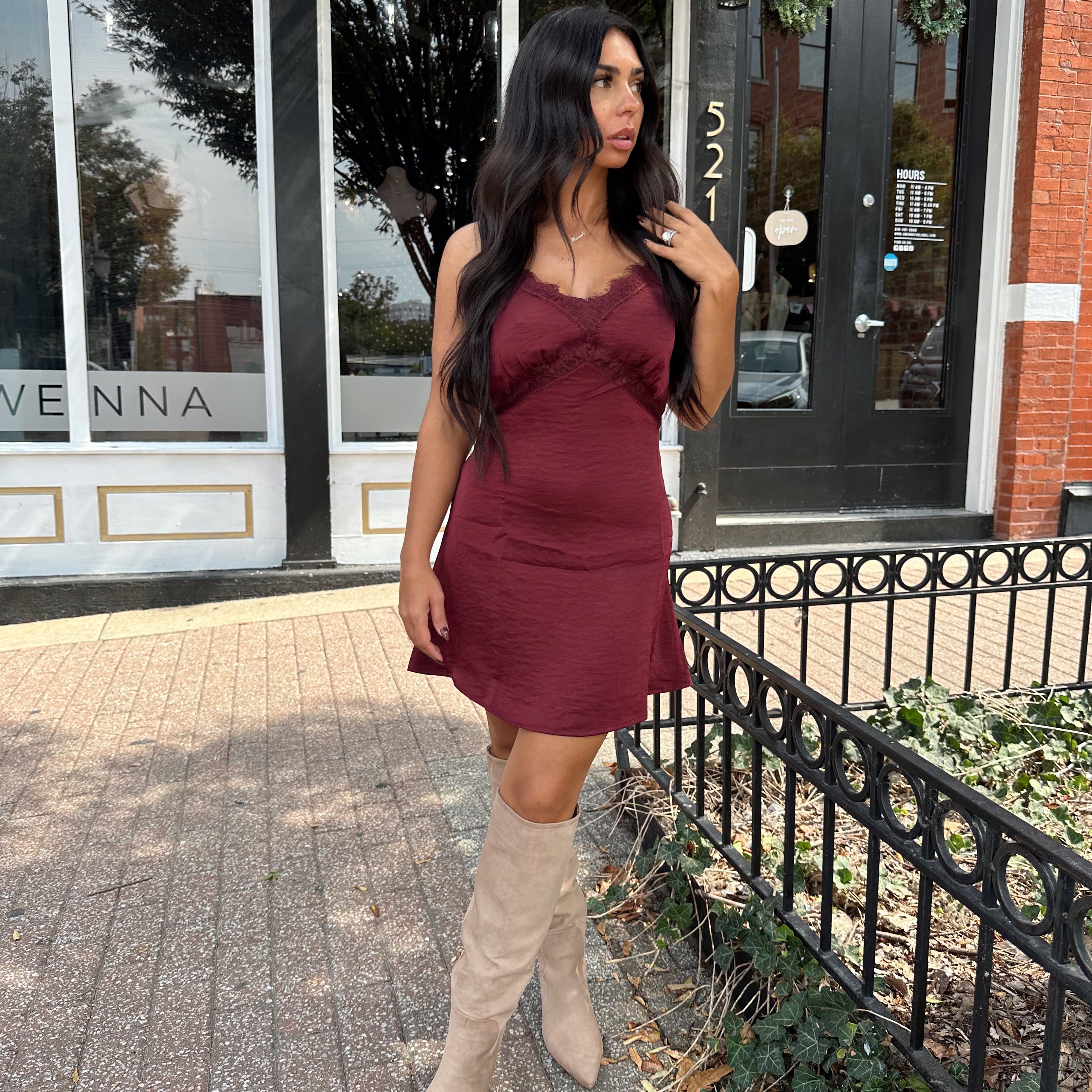 Woman wearing burgundy satin slip mini dress with lace detailing and adjustable straps.