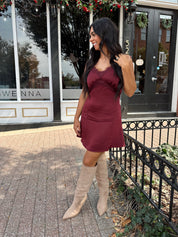 Woman wearing burgundy satin slip mini dress with lace detailing and adjustable straps.