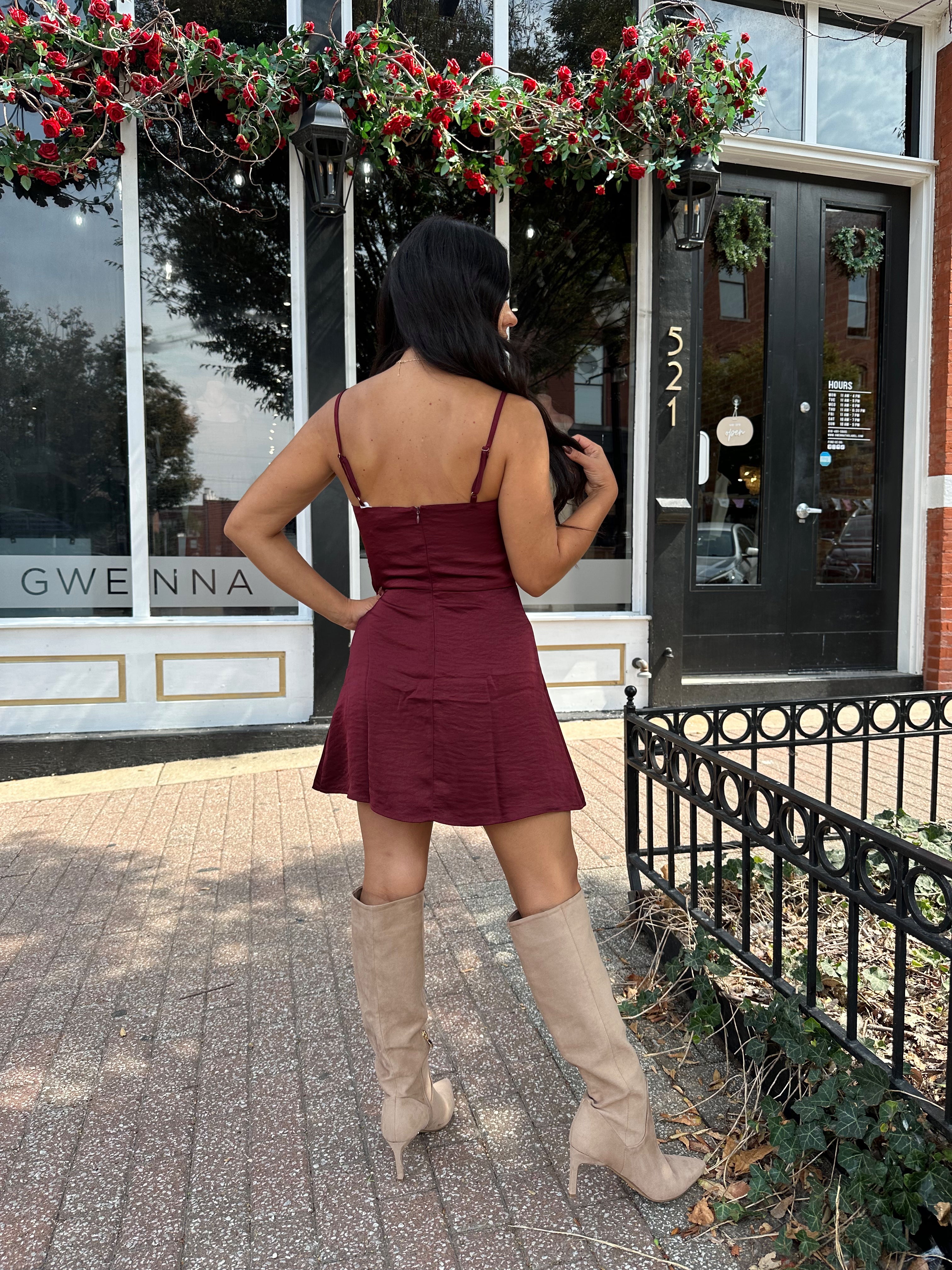 Woman wearing burgundy satin slip mini dress with lace detailing and adjustable straps.