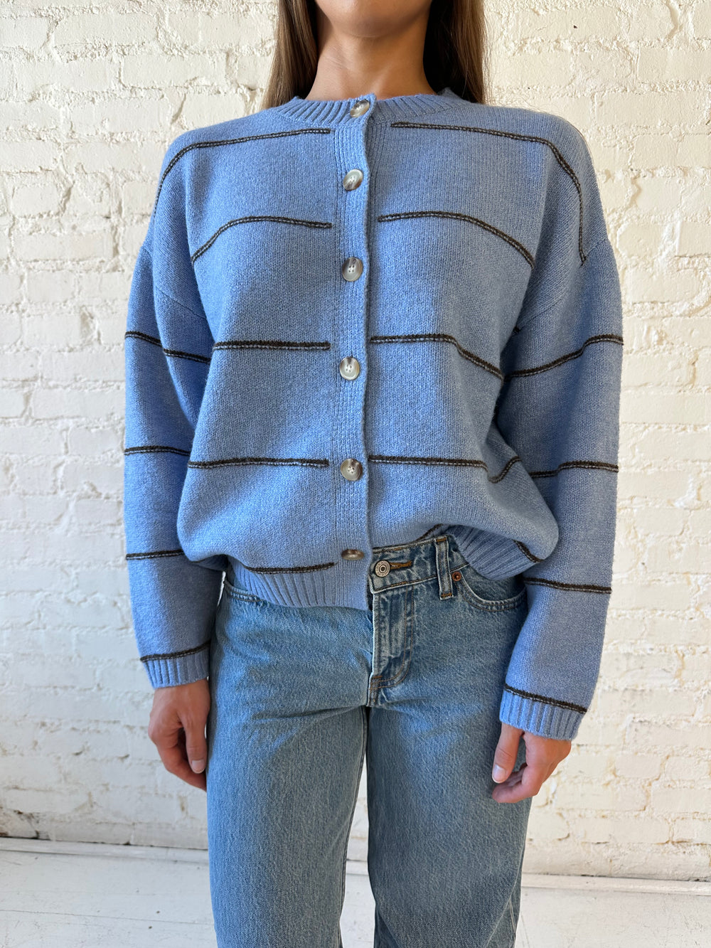 Woman wearing dusty blue striped button down cardigan with medium wash jean. 