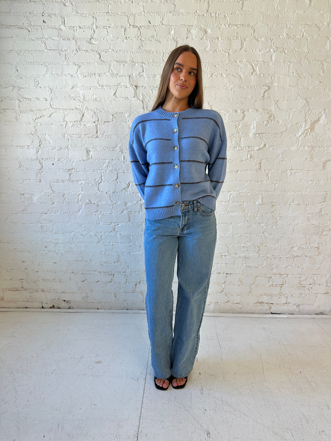 Woman wearing dusty blue striped button down cardigan with medium wash jean. 