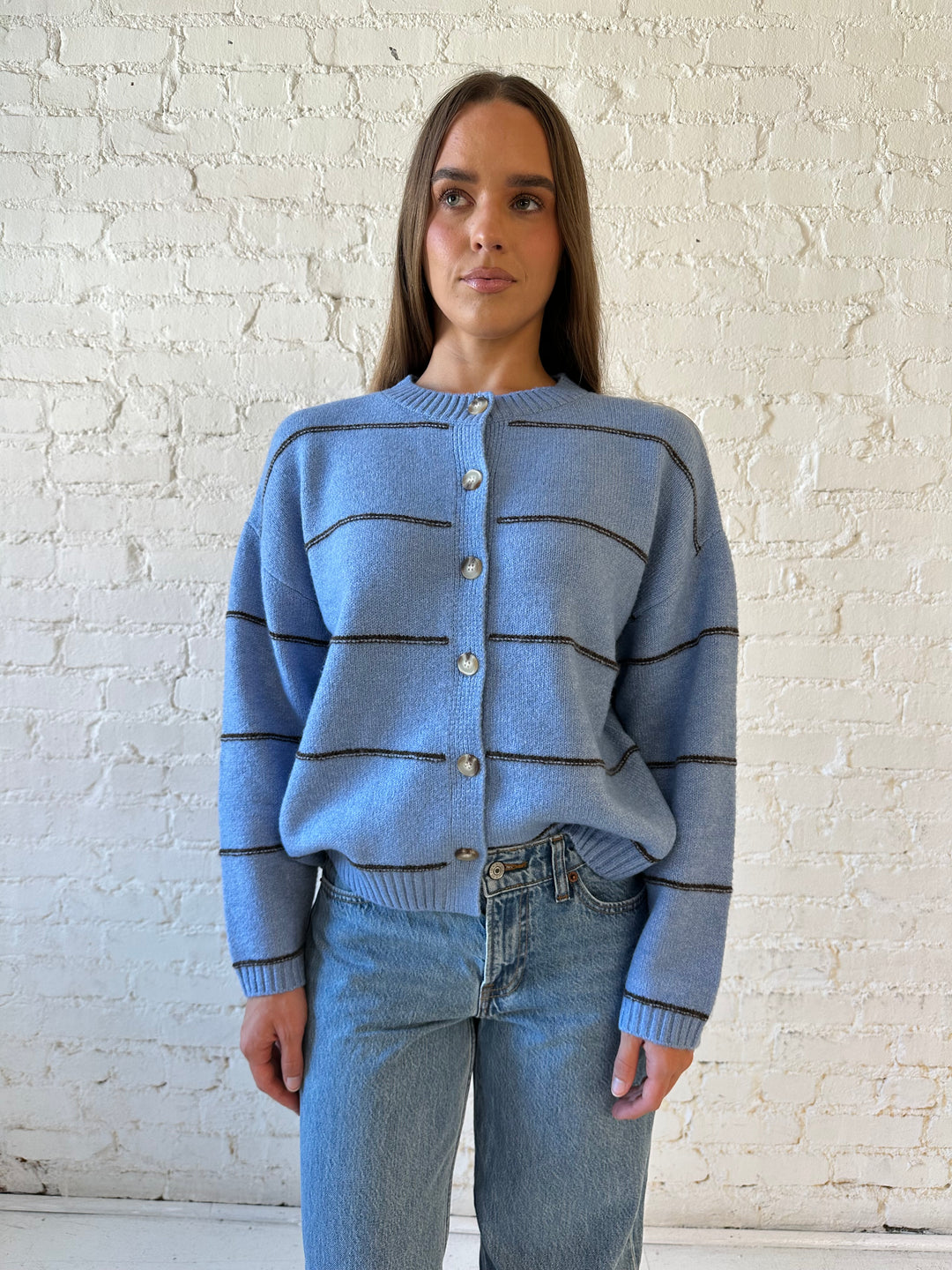 Woman wearing dusty blue striped button down cardigan with medium wash jean. 