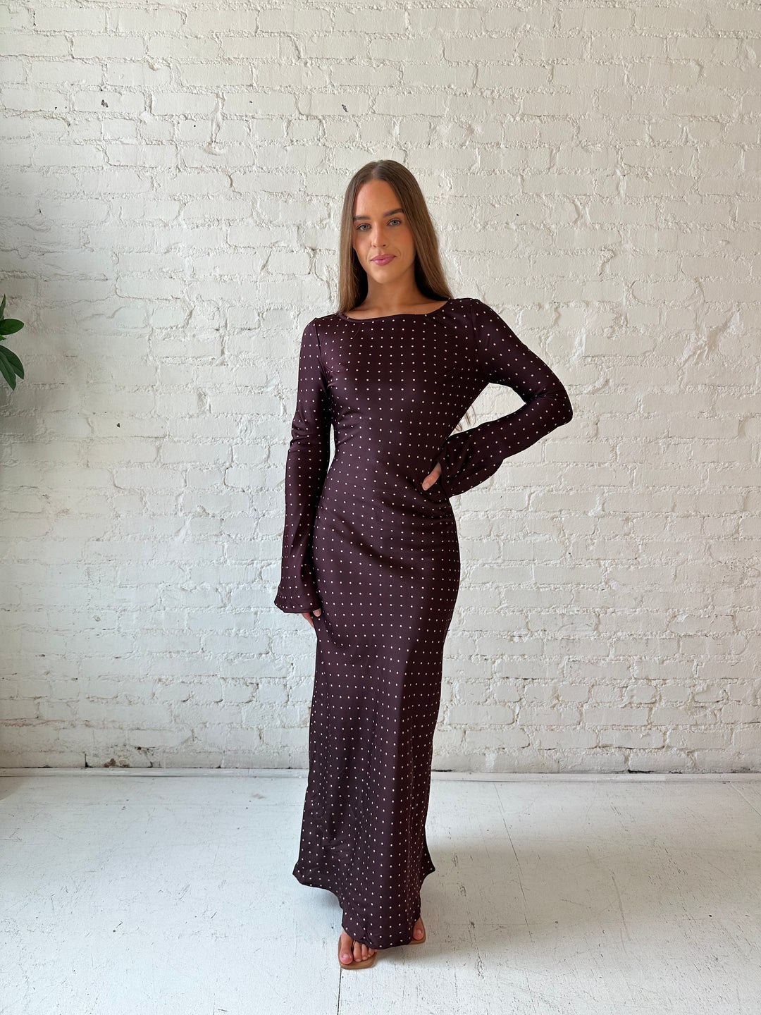 Woman wearing a burgundy polka dot  long sleeve satin maxi dress with heels.