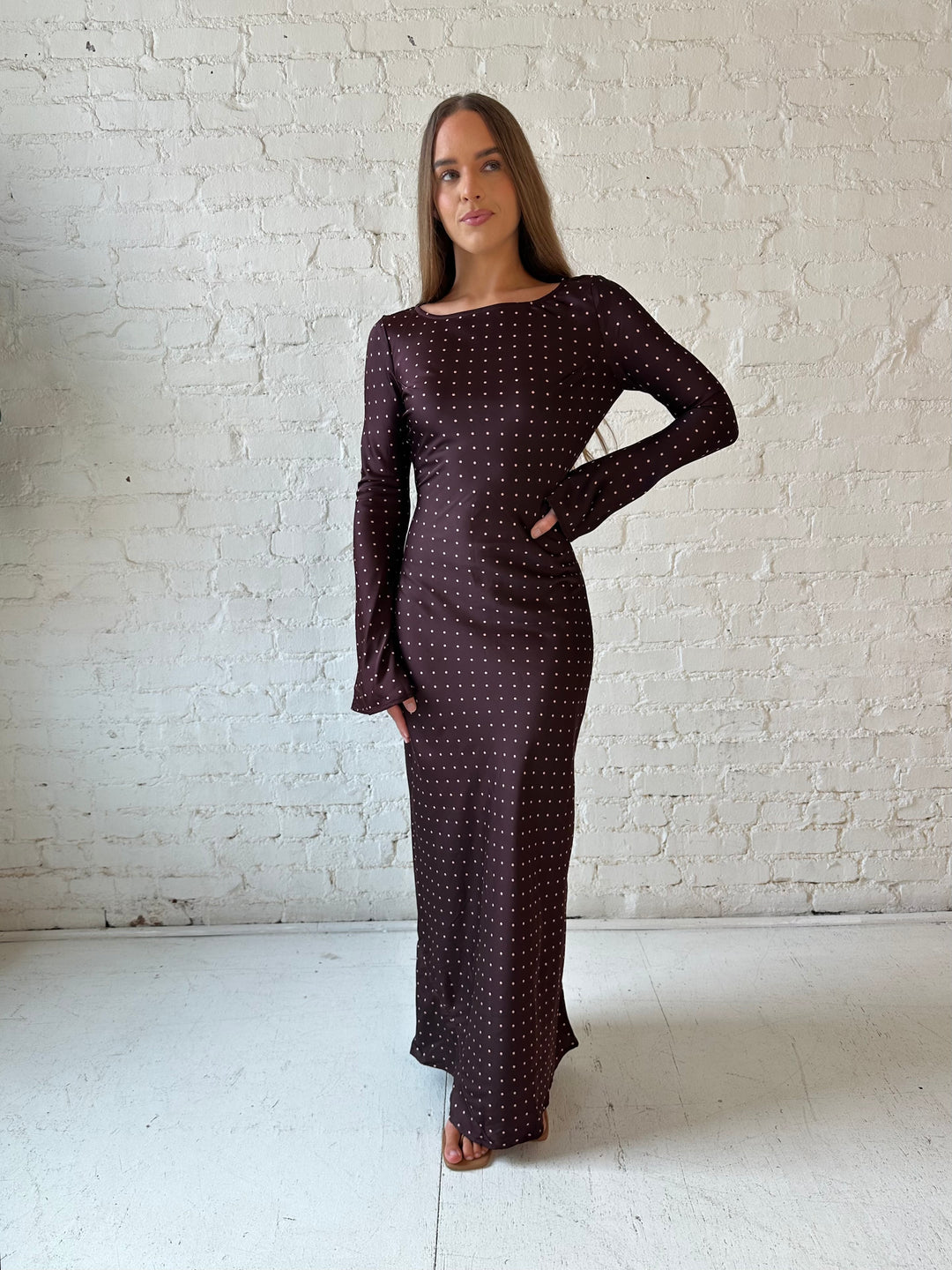 Woman wearing a burgundy polka dot  long sleeve satin maxi dress with heels.
