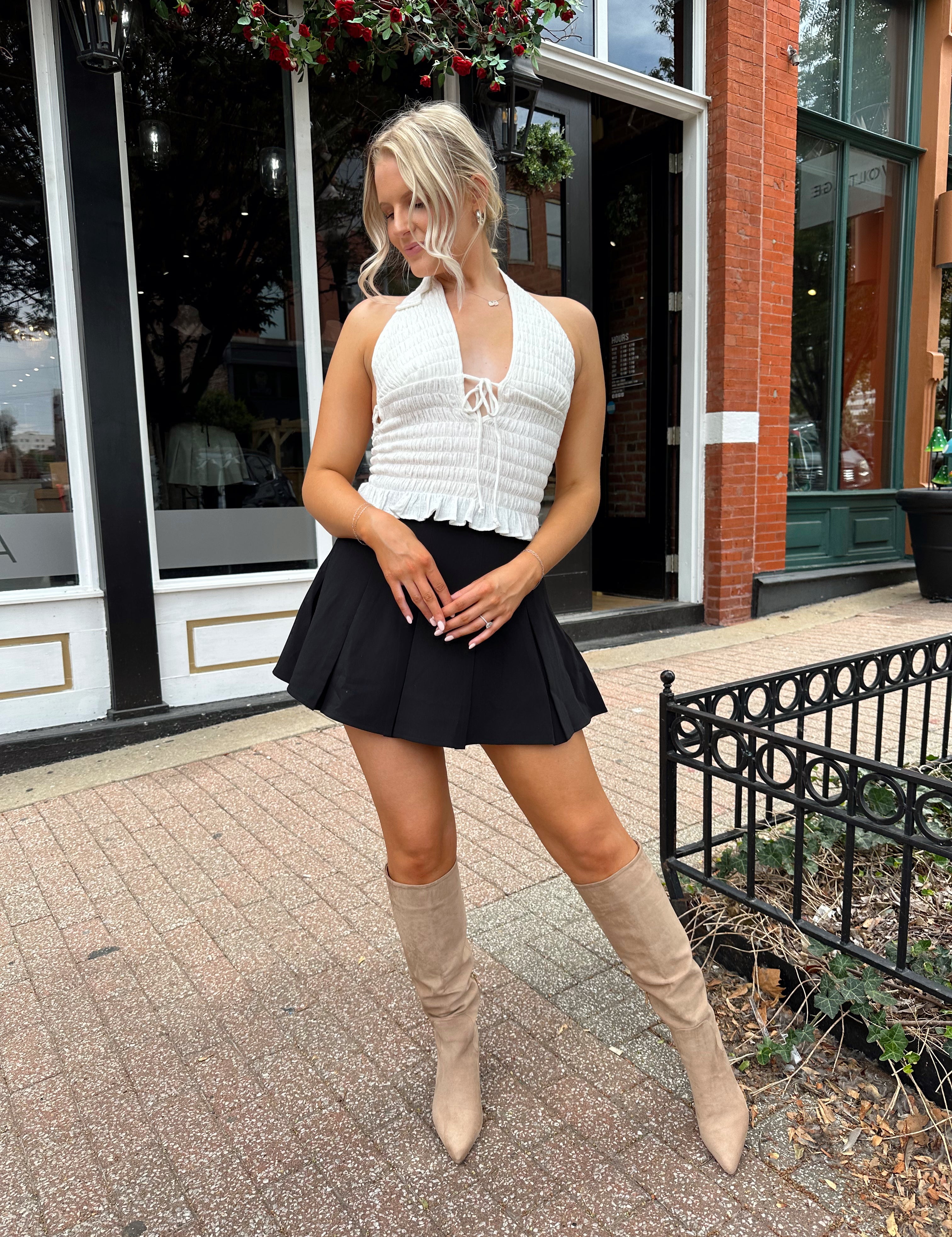 Woman wearing white smocked halter top with black mini skirt and black blazer. 