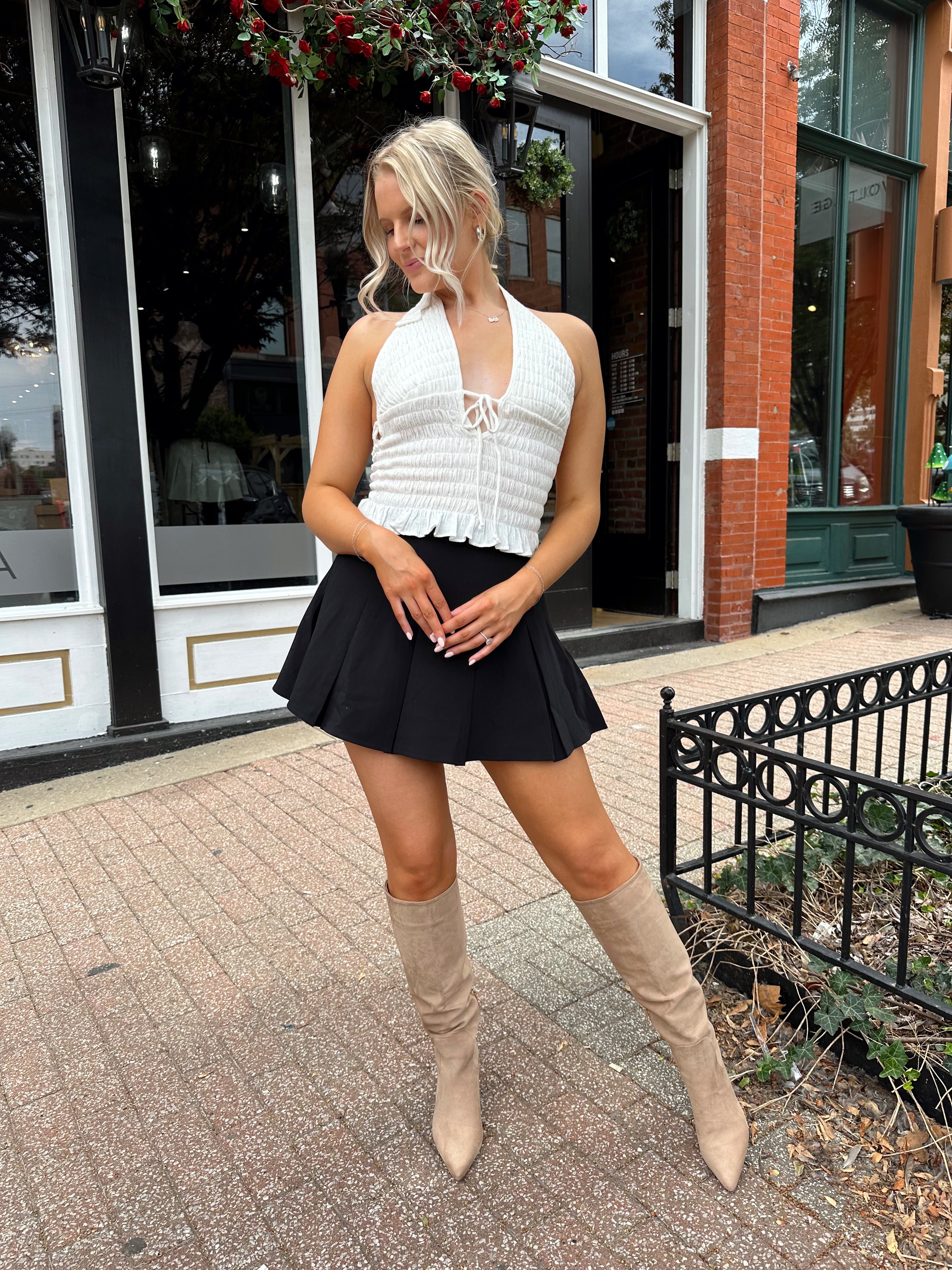 Woman wearing white smocked halter top with black mini skirt and black blazer. 