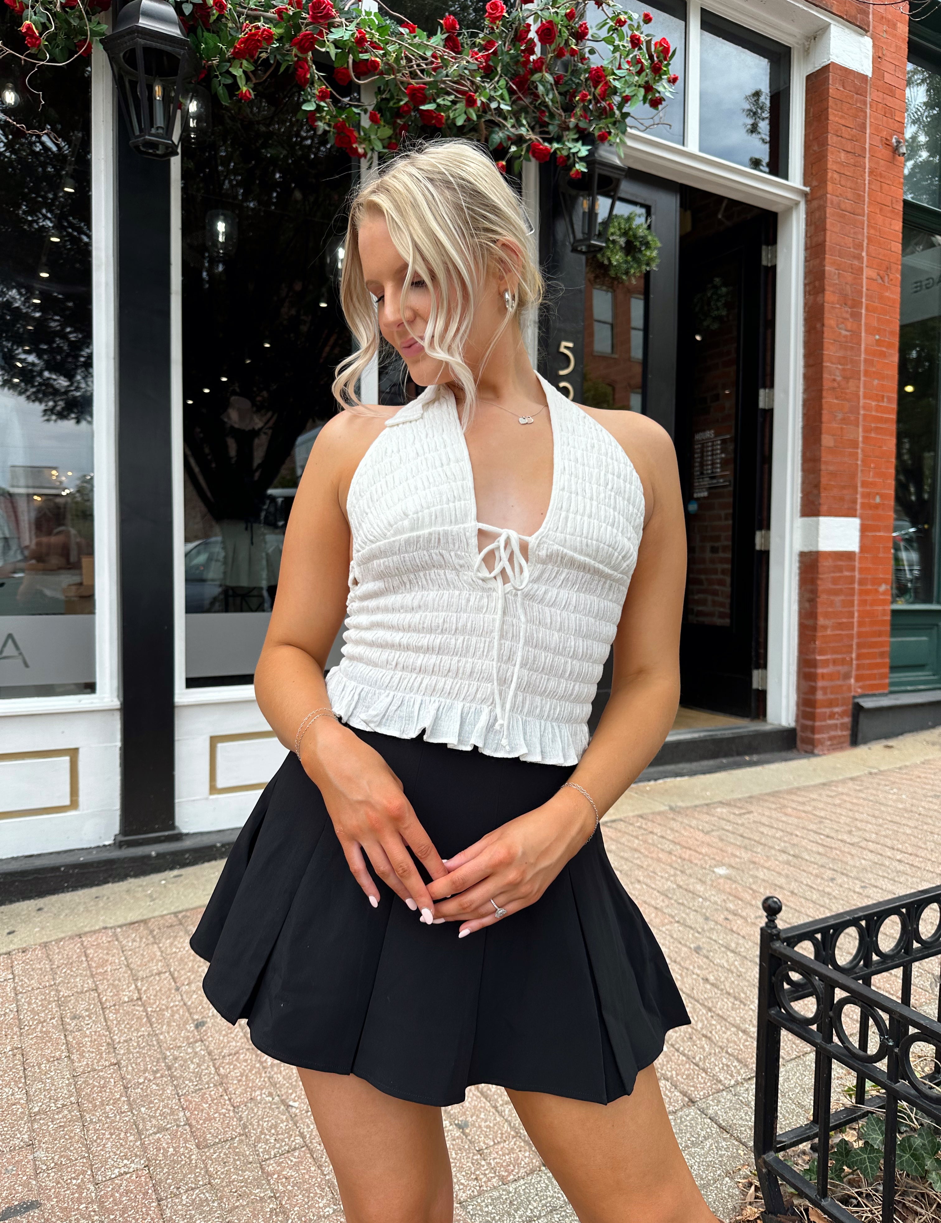 Woman wearing white smocked halter top with black mini skirt and black blazer. 