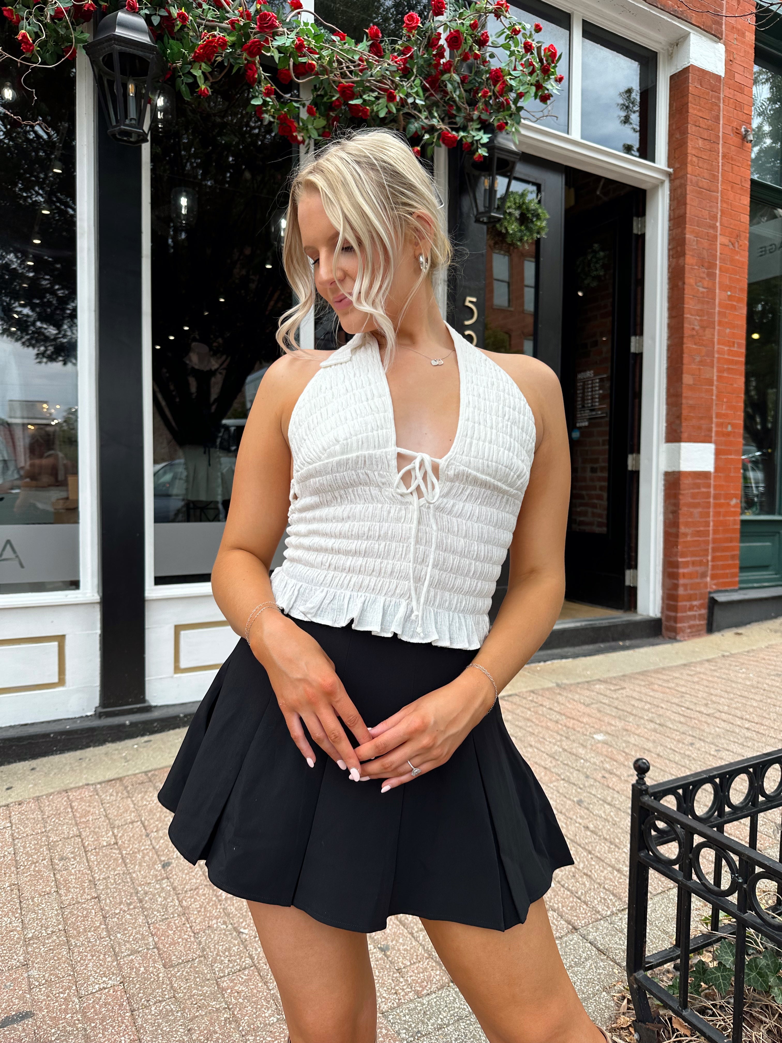 Woman wearing white smocked halter top with black mini skirt and black blazer. 