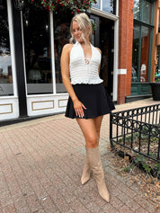 Woman wearing white smocked halter top with black mini skirt and black blazer. 