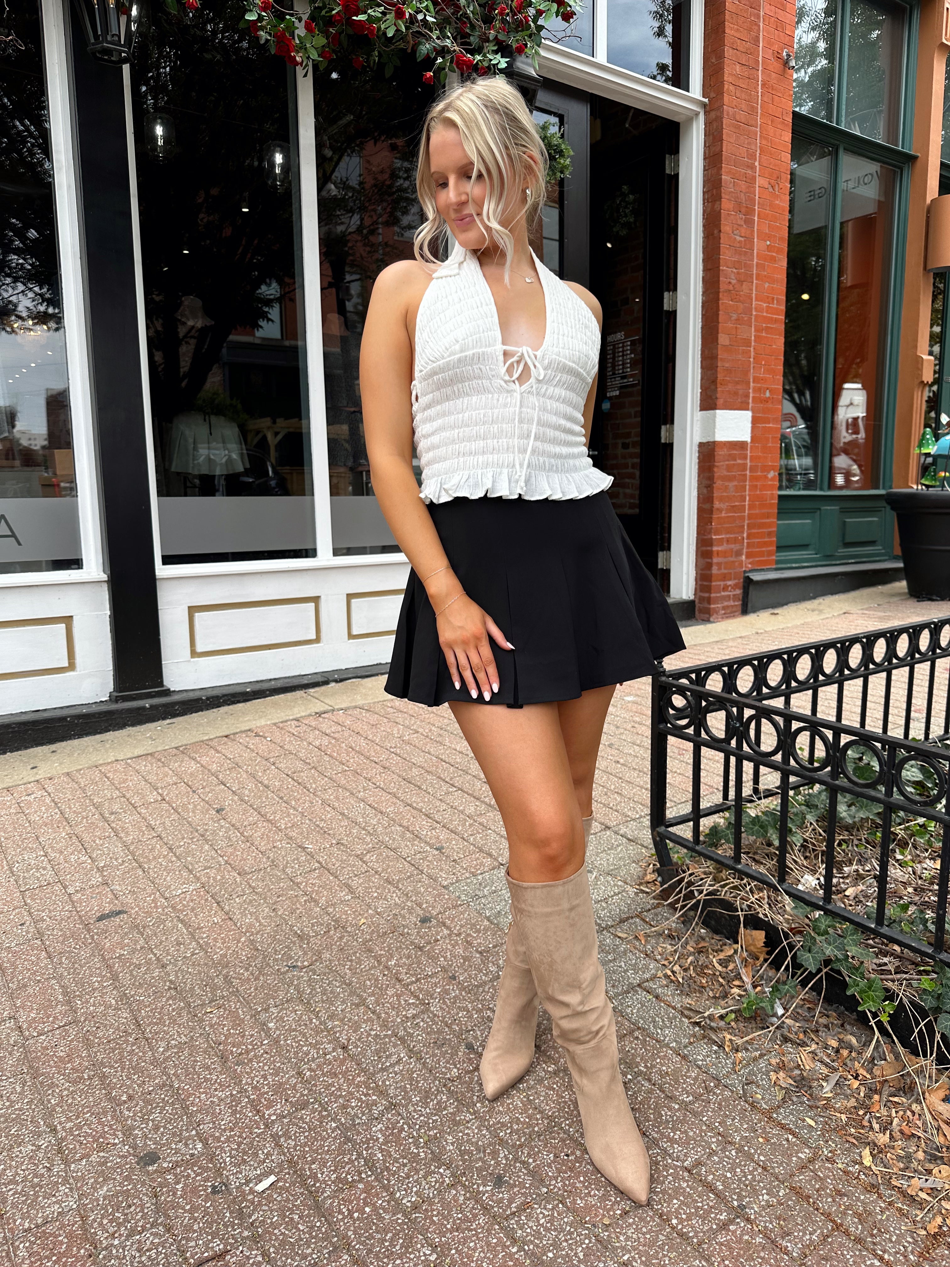 Woman wearing white smocked halter top with black mini skirt and black blazer. 