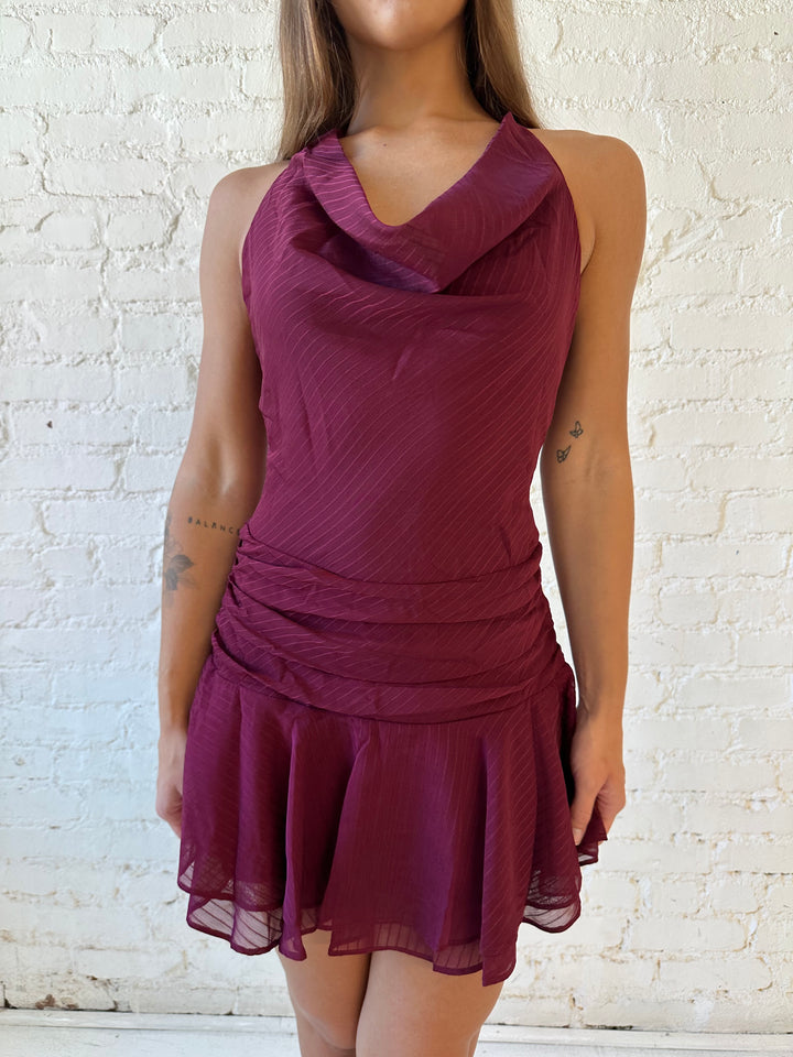 Woman wearing burgundy striped mini dress with a cowl, self tie halter neckline and low back.