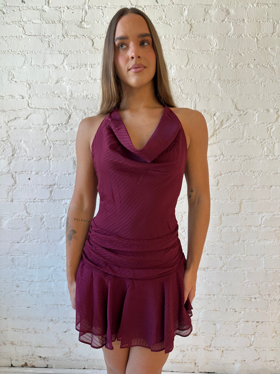 Woman wearing burgundy striped mini dress with a cowl, self tie halter neckline and low back.