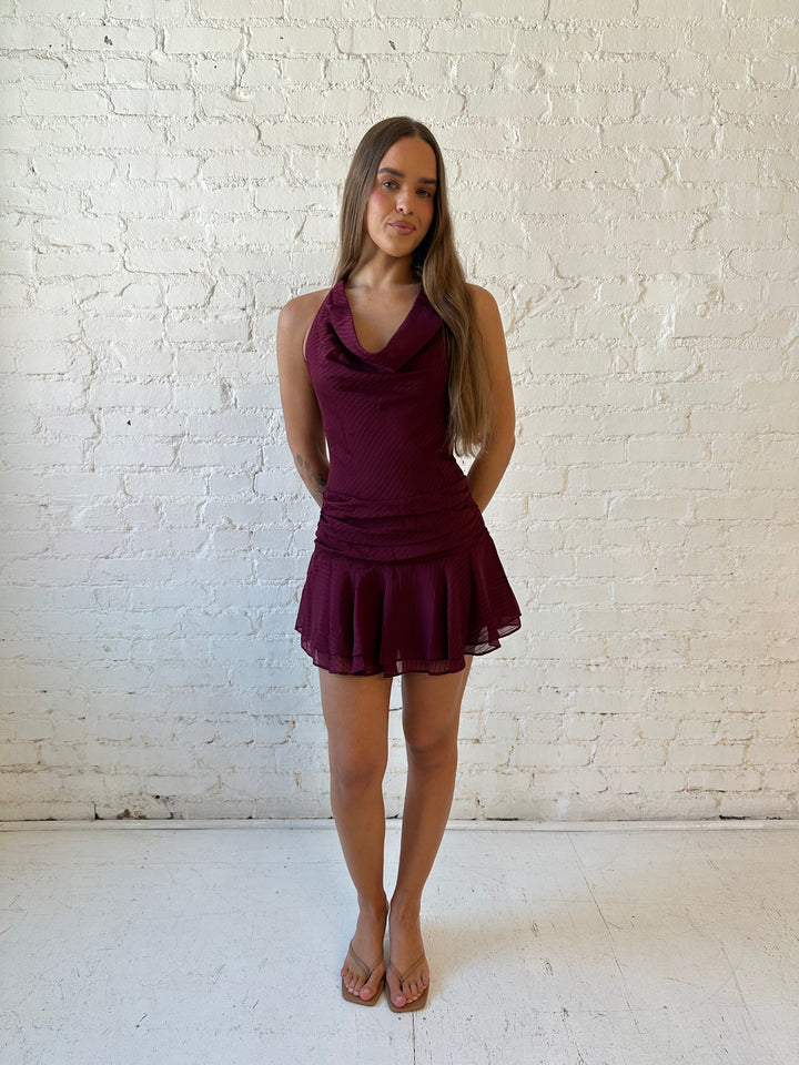 Woman wearing burgundy striped mini dress with a cowl, self tie halter neckline and low back.