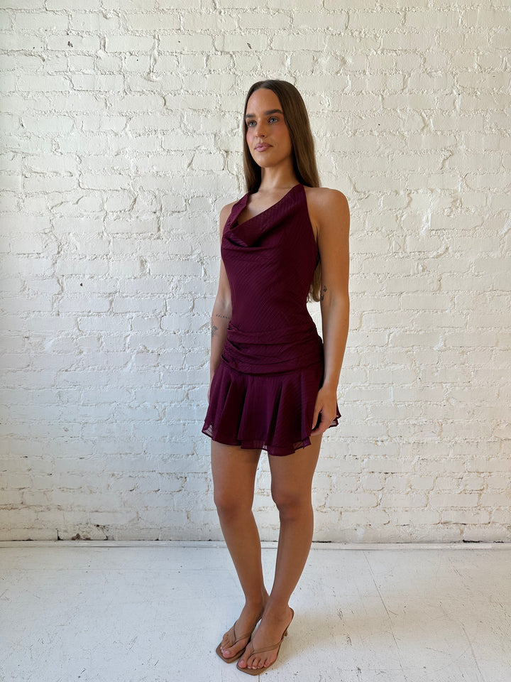 Woman wearing burgundy striped mini dress with a cowl, self tie halter neckline and low back.