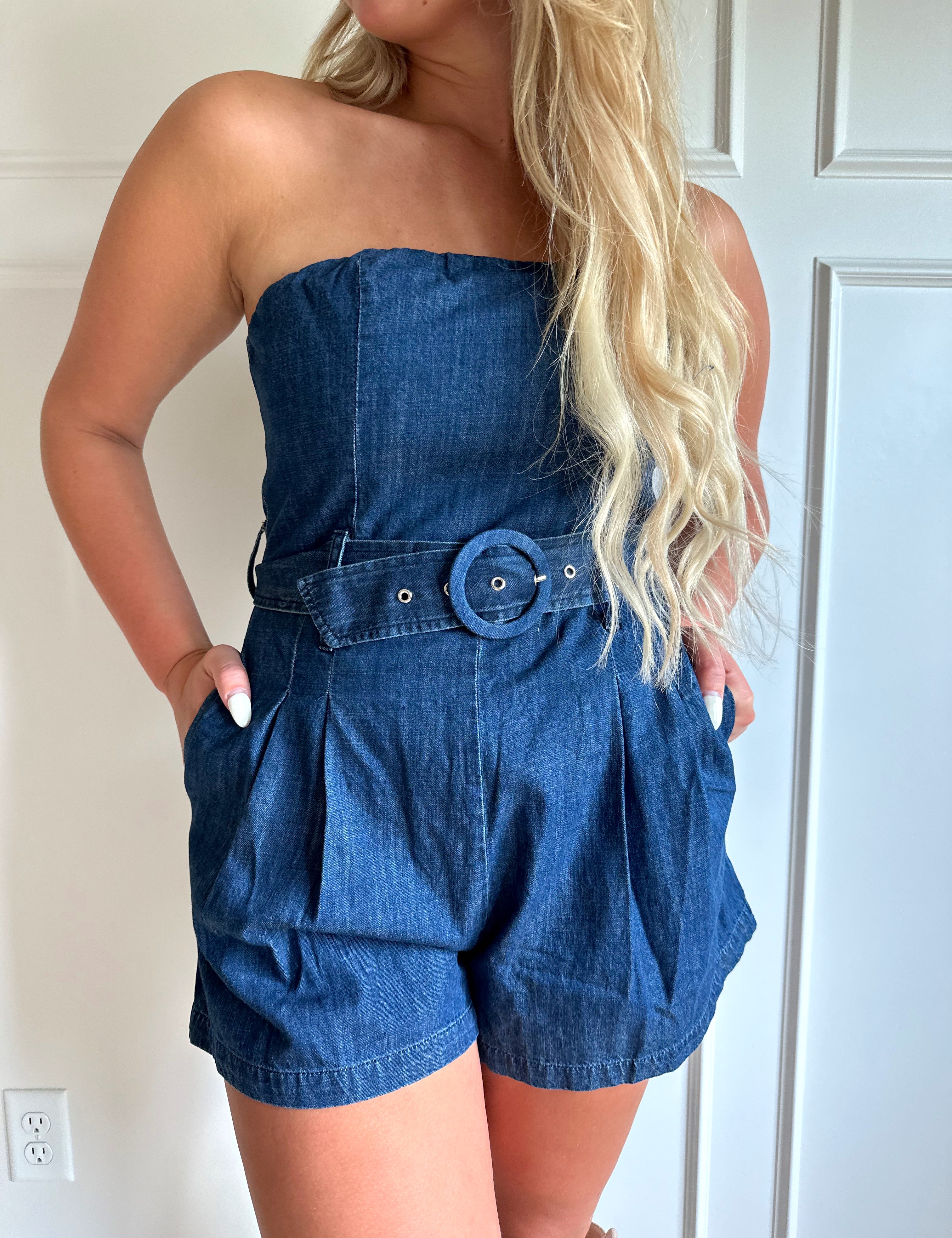 Woman wearing a dark wash strapless denim romper with a belted waist, and functional pockets.