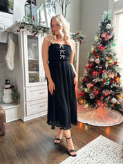 Woman wearing black sparkle midi dress with rhinestone bow detailing. 